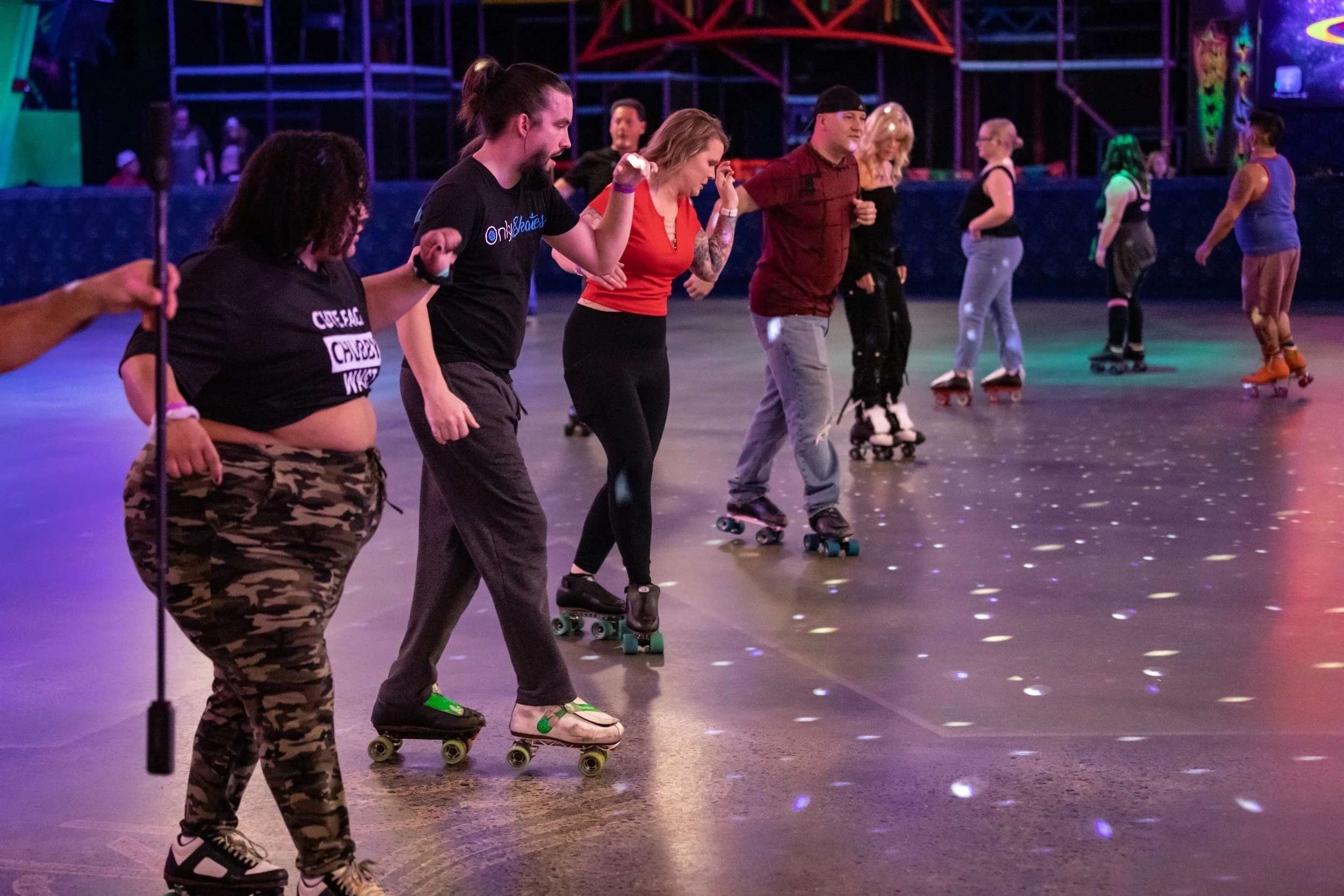 People roller skating in an indoor rink under colorful lighting.