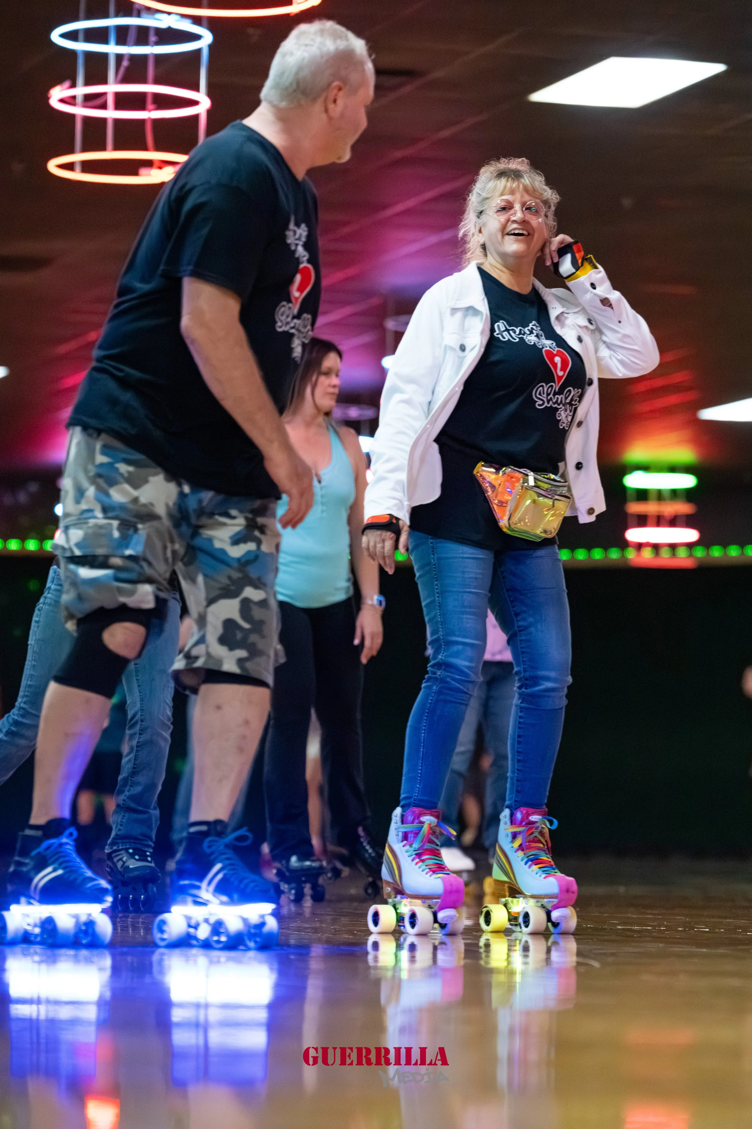 People roller skating indoors with colorful neon lights overhead, enjoying the activity.