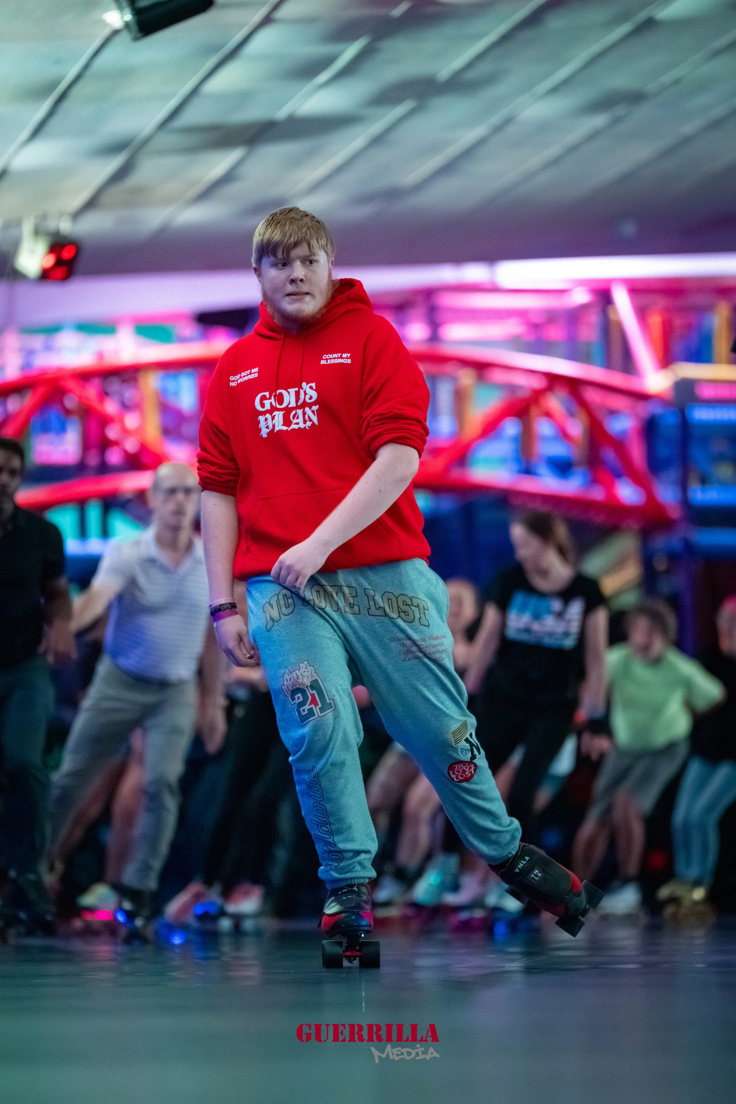 A young man rollerblading indoors with a group of people behind him, in a brightly lit arcade or entertainment venue with colorful neon lights.