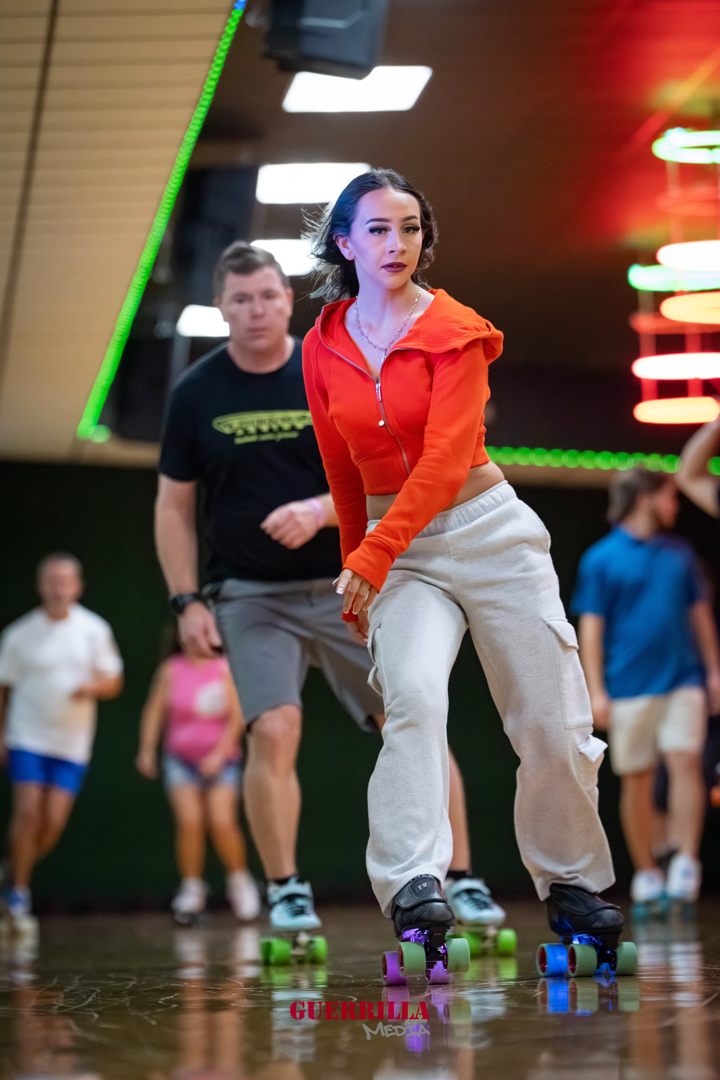 Young woman roller skating indoors with a group of people in the background.