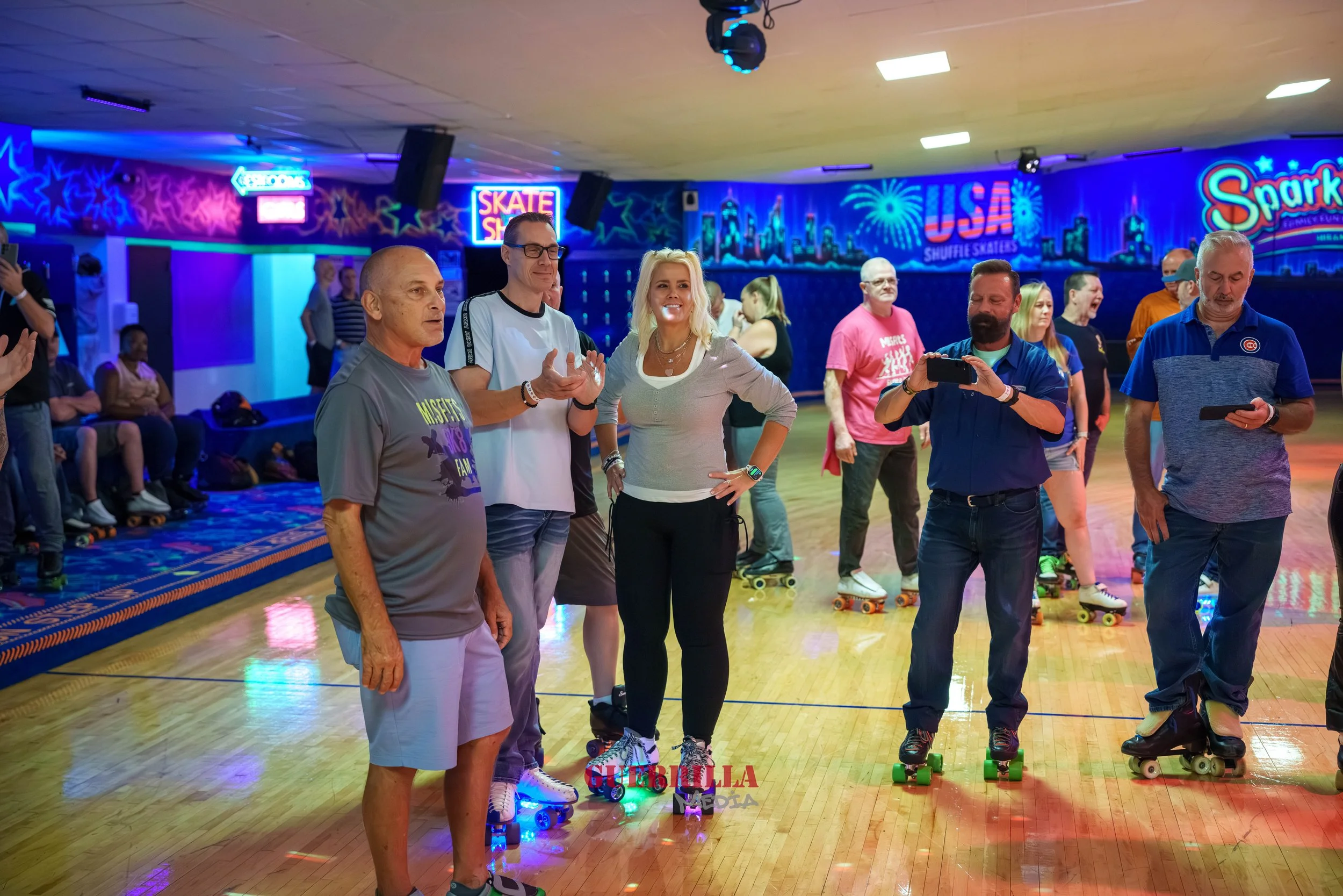 People roller skating in a brightly lit roller rink with colorful neon signs and cityscape mural on the wall.