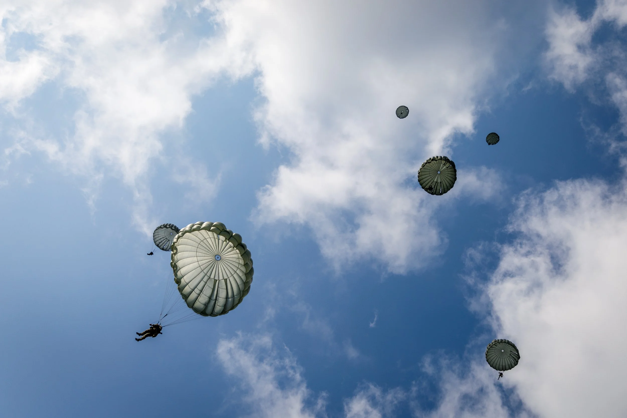 Paratroopers descending with parachutes in a blue sky with clouds.