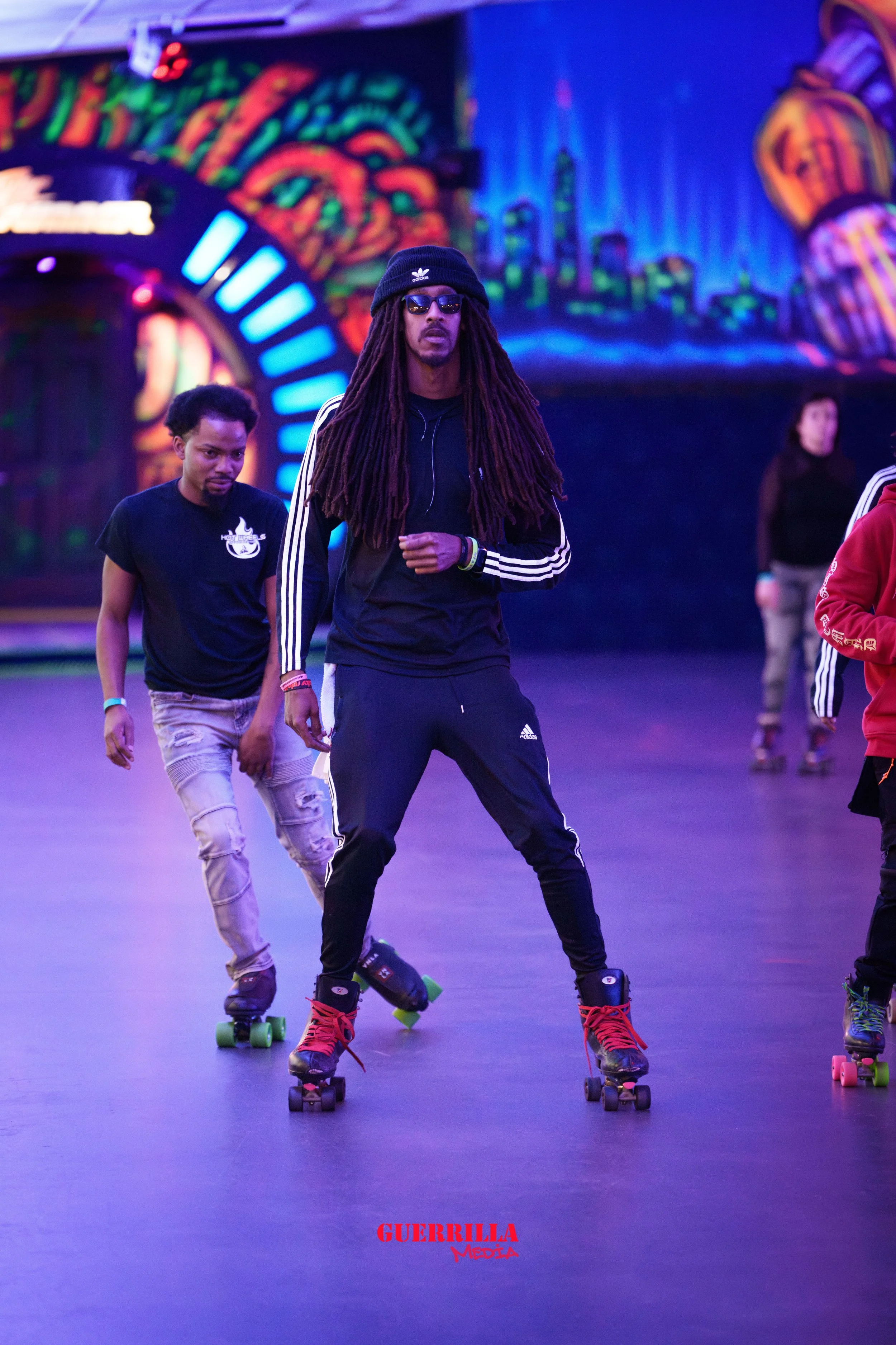Group of people roller skating indoors with illuminated, colorful graffiti-style wall art in the background.