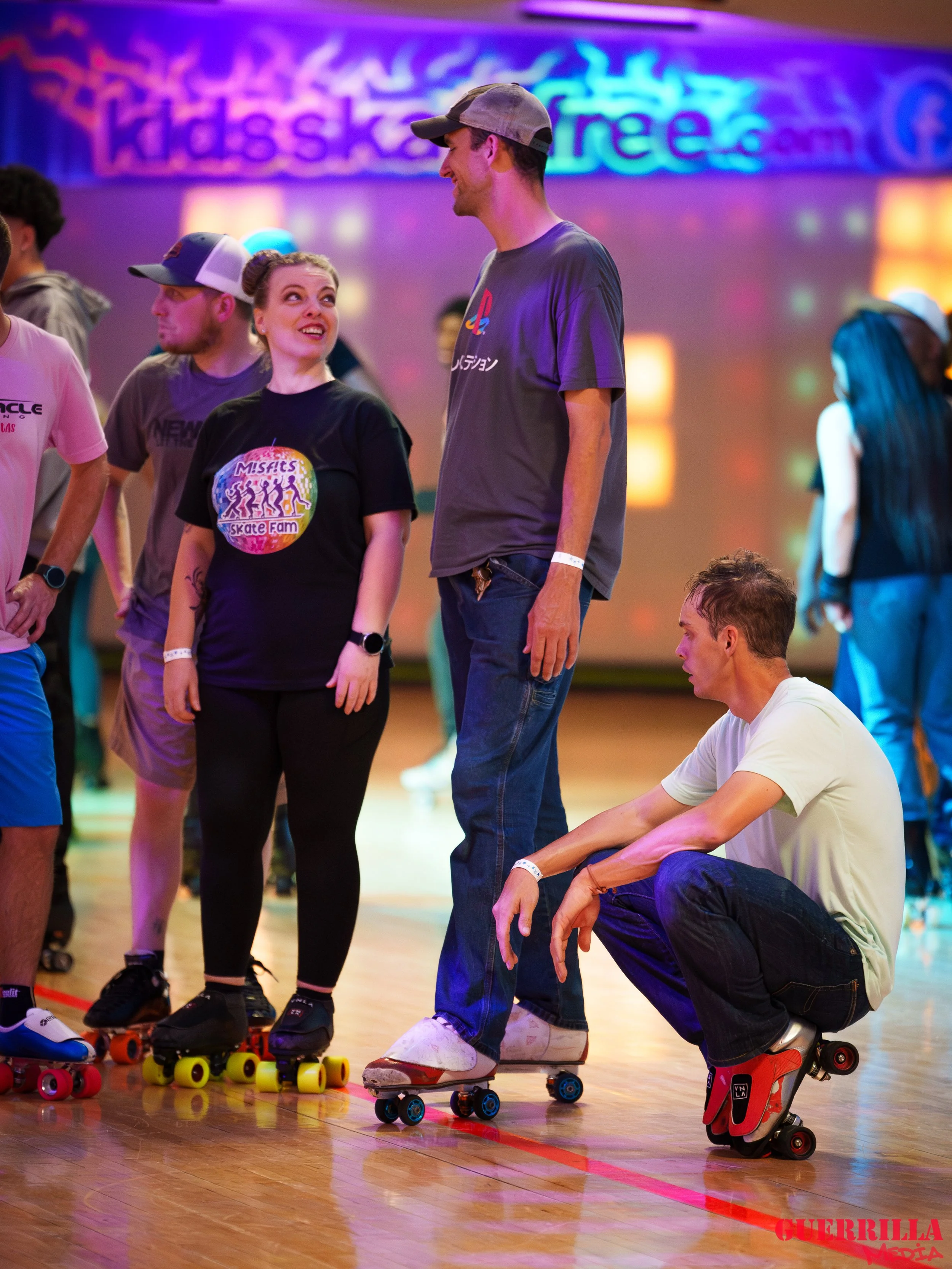 A group of people roller skating indoors at an event, with colorful lighting and banners in the background.