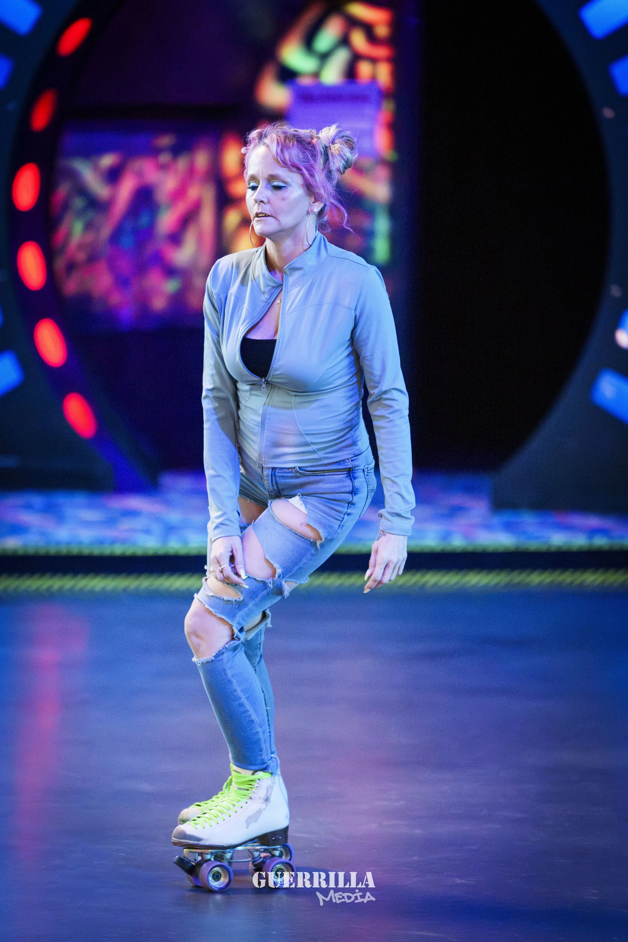 A woman with pink and purple hair roller-skates on a shiny floor, wearing a gray jacket, ripped jeans, and neon green laces, with colorful neon lights in the background.
