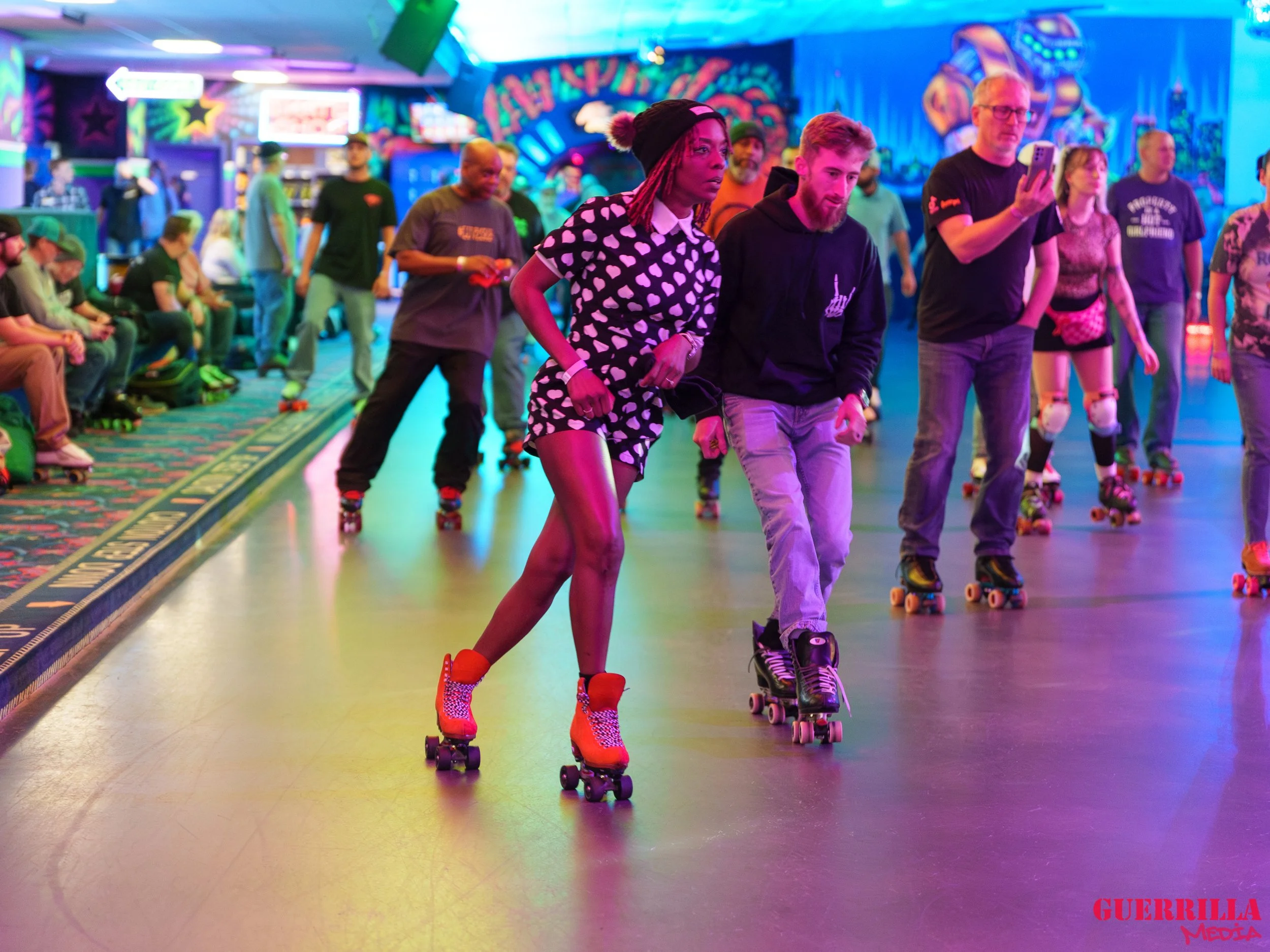 People roller skating in an indoor roller rink with colorful lights and neon decorations, some are sitting and watching.