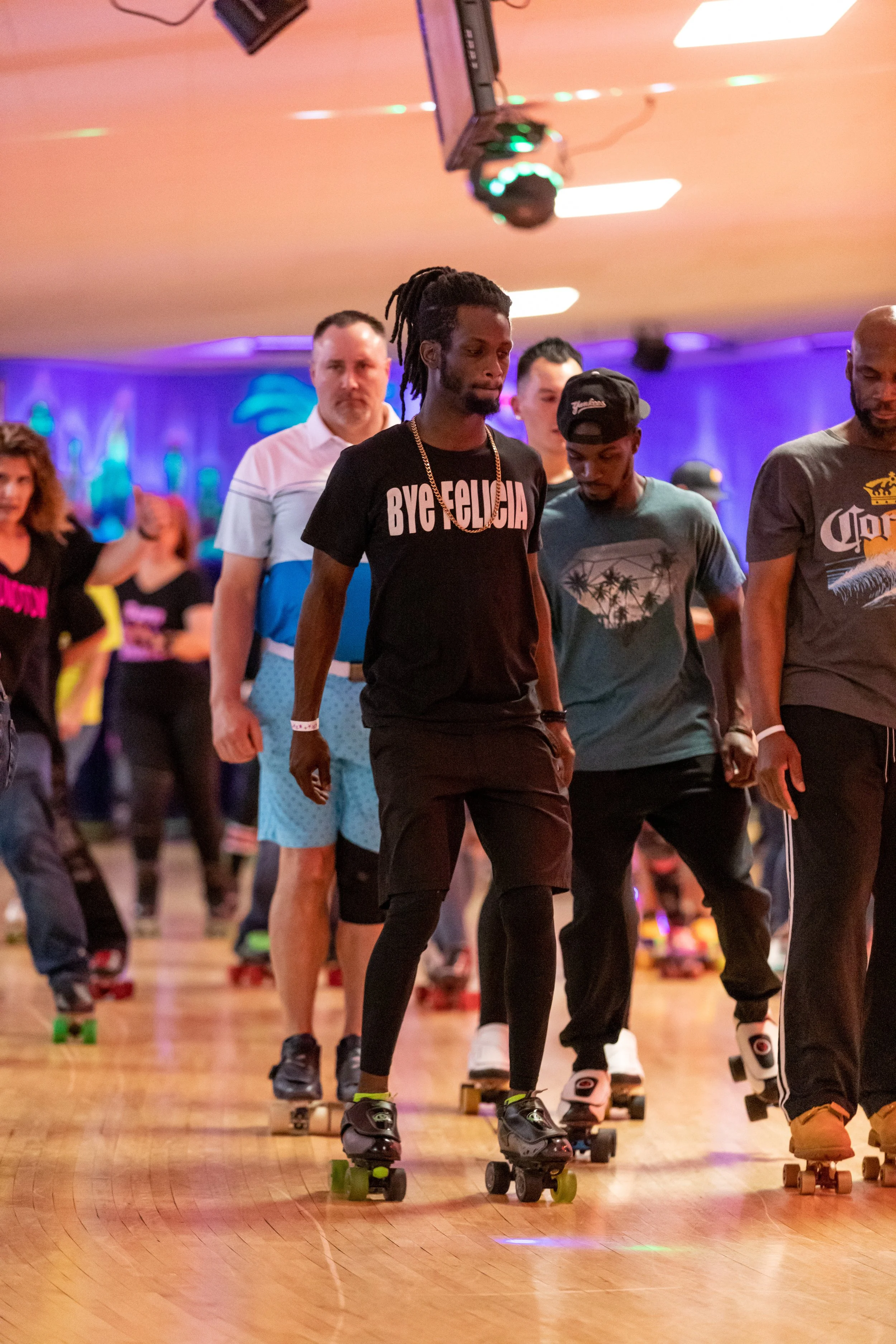 People roller skating in an indoor rink with colorful lighting.