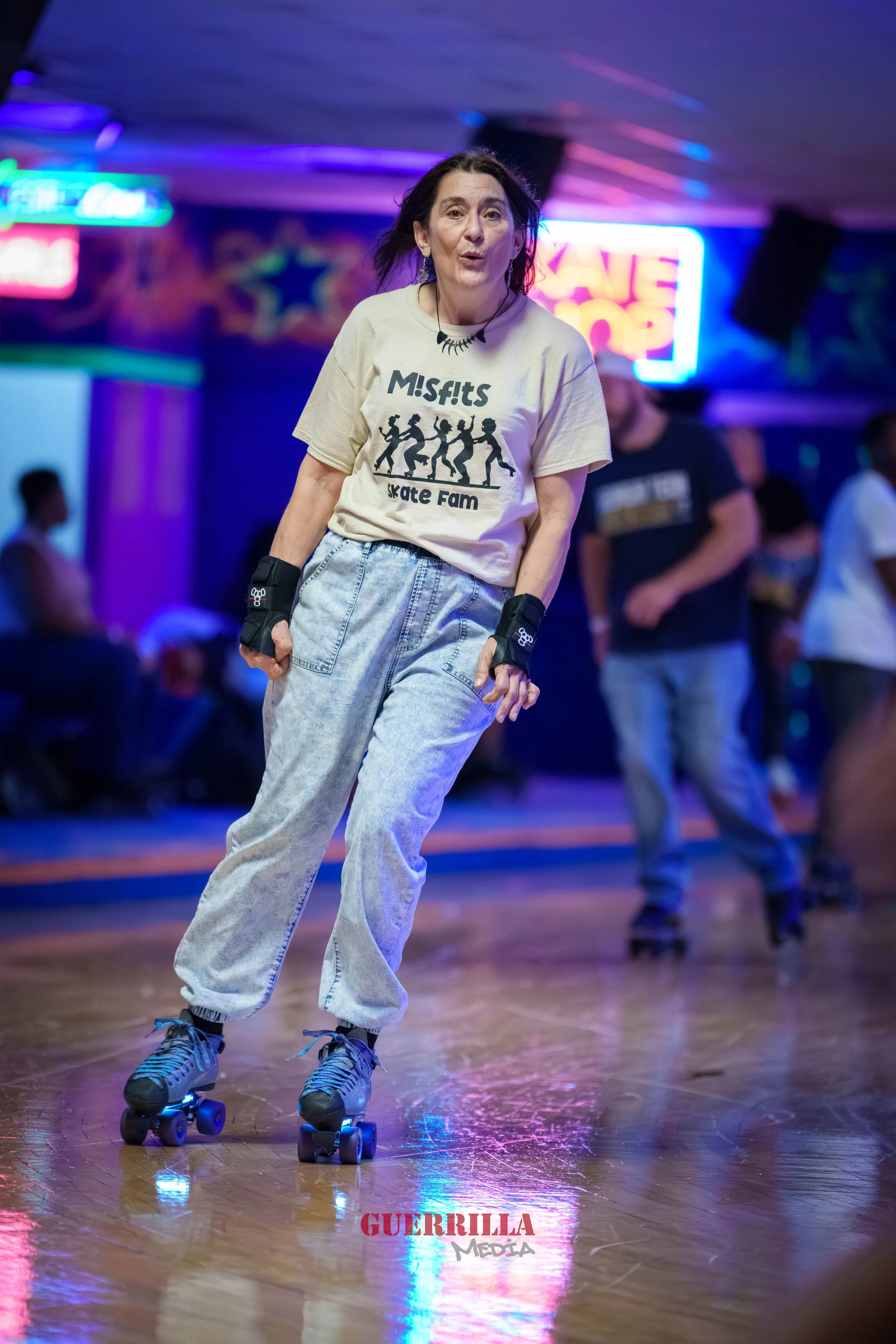Woman roller skating in a neon-lit dance rink, wearing a Misfits skateboard t-shirt and loose jeans.