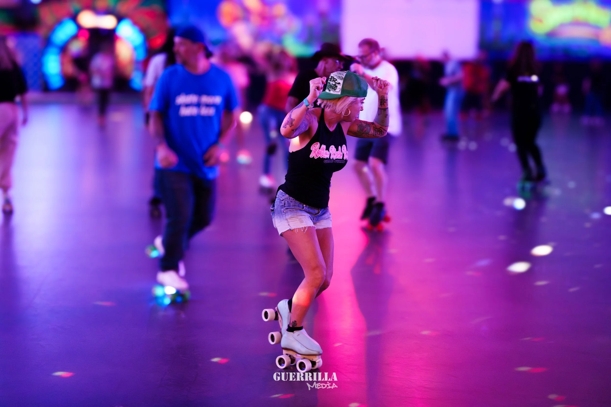 A woman roller skating in a neon-lit indoor roller rink with colorful, blurred background and other skaters around her.