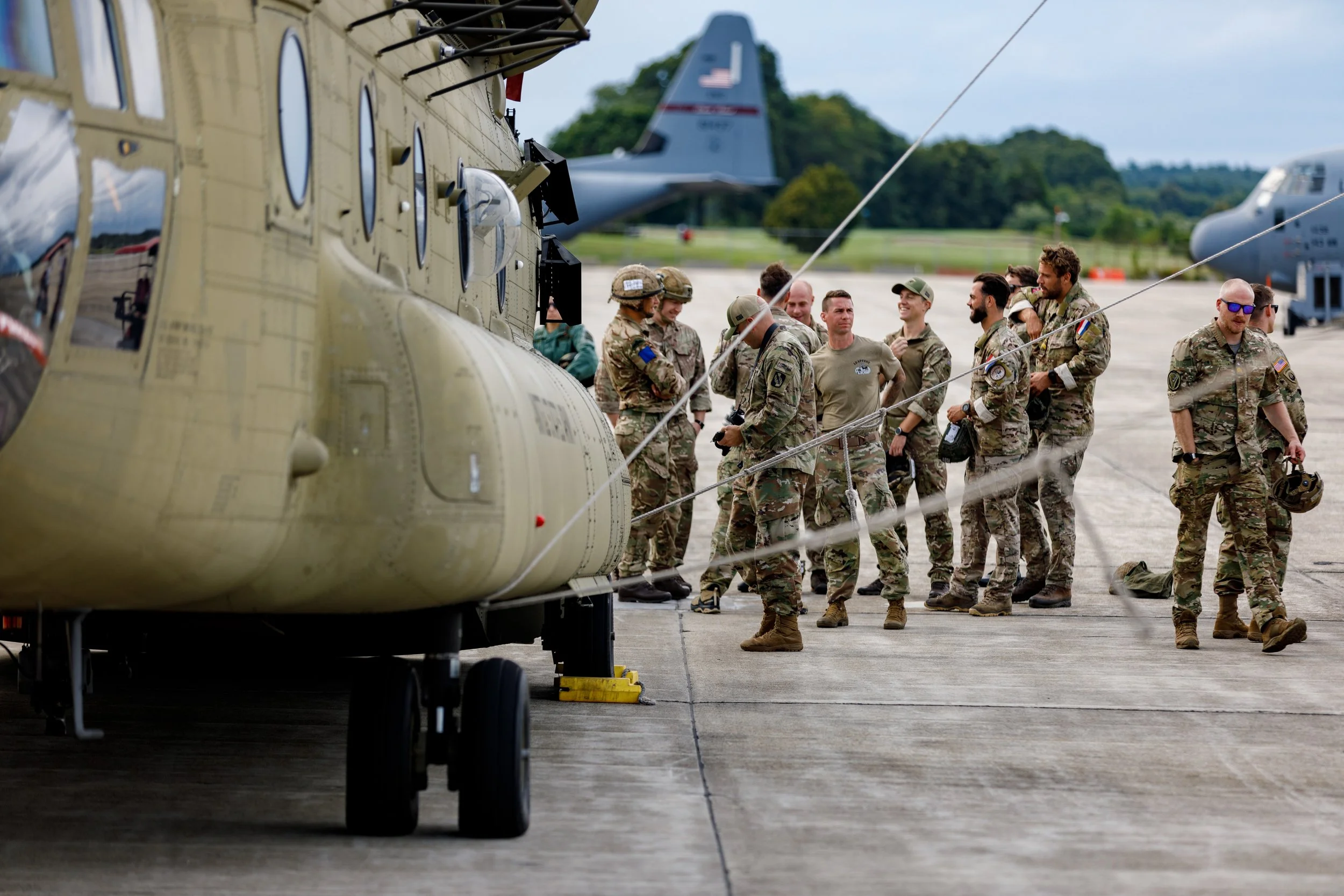 Group of soldiers gathering on a tarmac near military helicopters and aircraft.