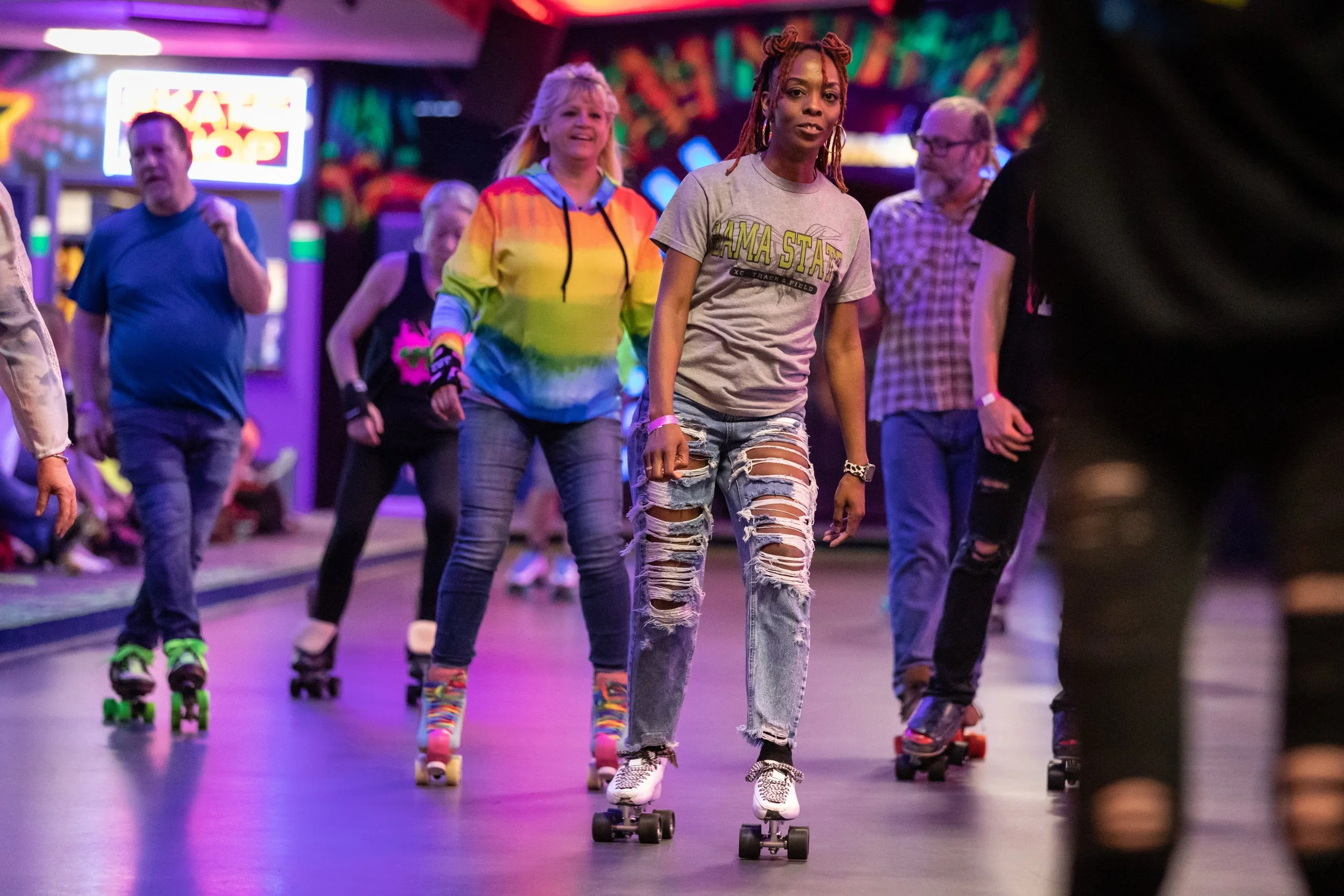 People roller skating in an indoor rink with colorful lighting and graffiti-style wall art.