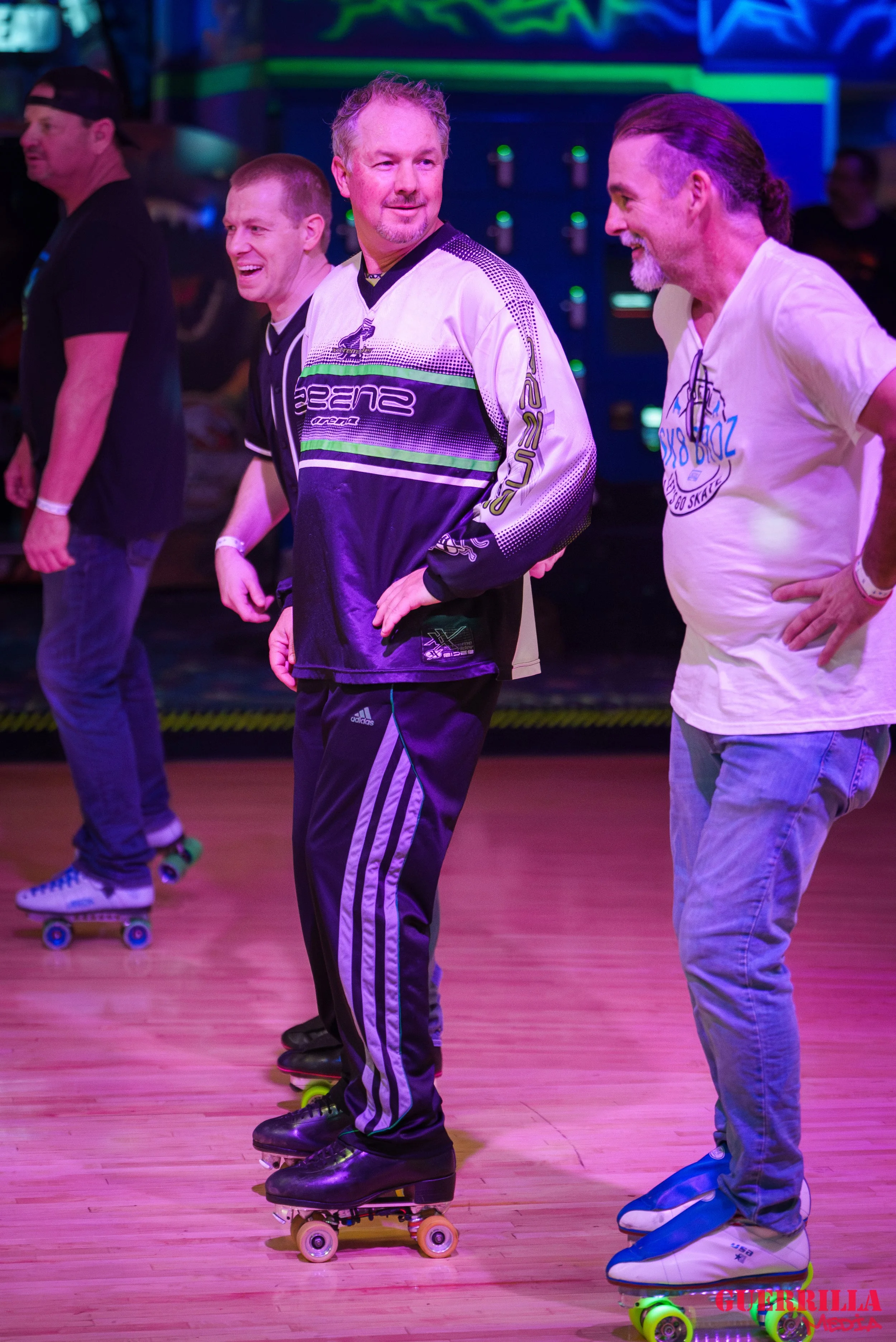 A group of men roller skating indoors, smiling and socializing under colorful lighting.