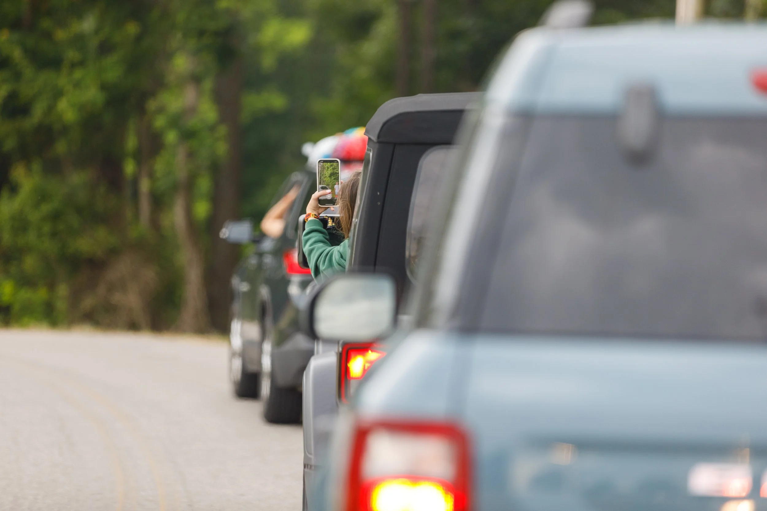 People in a line of cars on a road, with one person taking a photo with a smartphone while sitting in a vehicle.