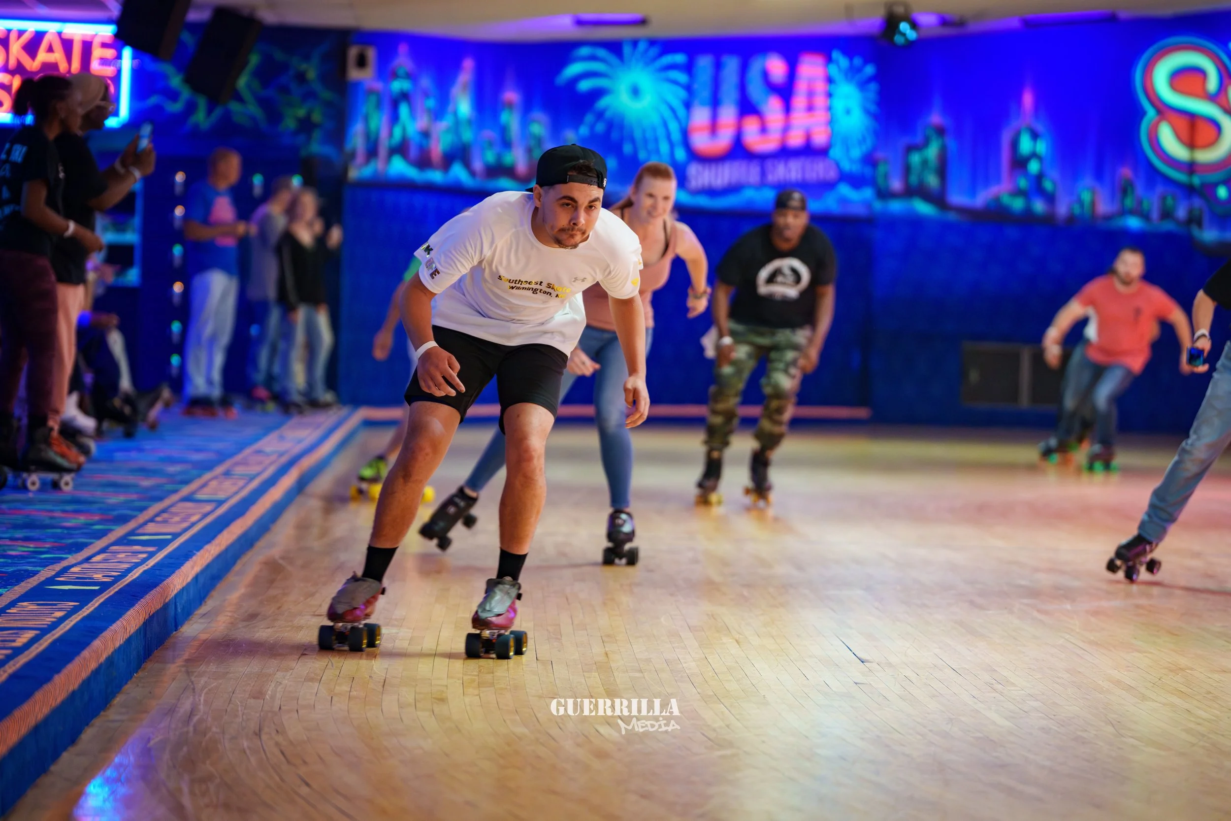 People roller skating in a brightly lit indoor skating rink with neon signs and colorful decorations.