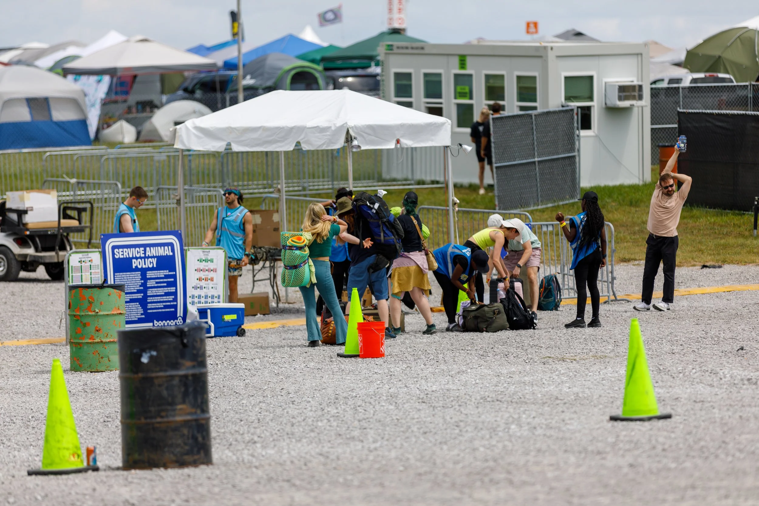 People standing in line at a service animal policy check-in area outdoors during a festival or event, with tents and temporary structures in the background.