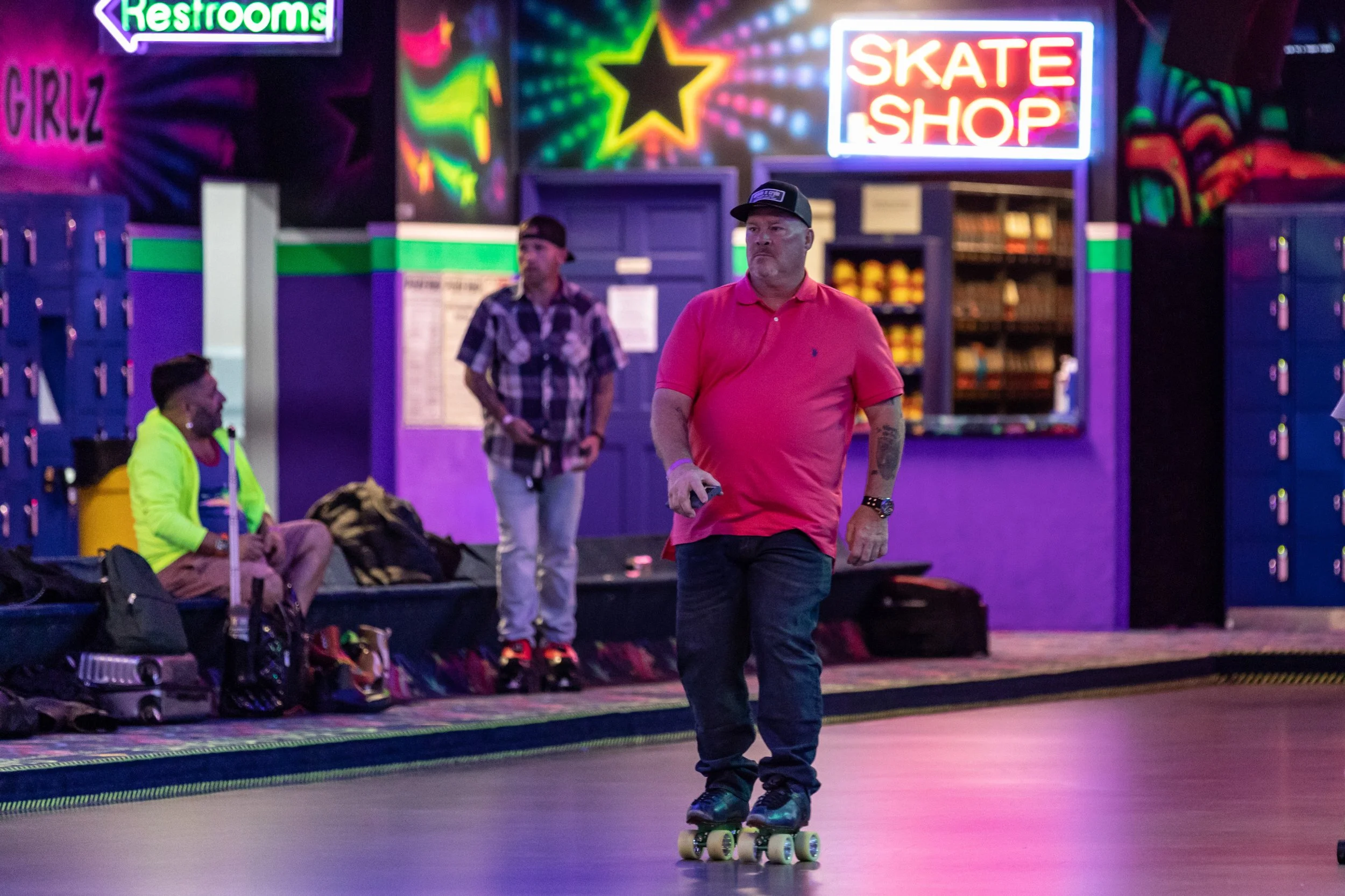 Man skateboarding at an indoor roller skating rink with neon signs and lockers in the background.