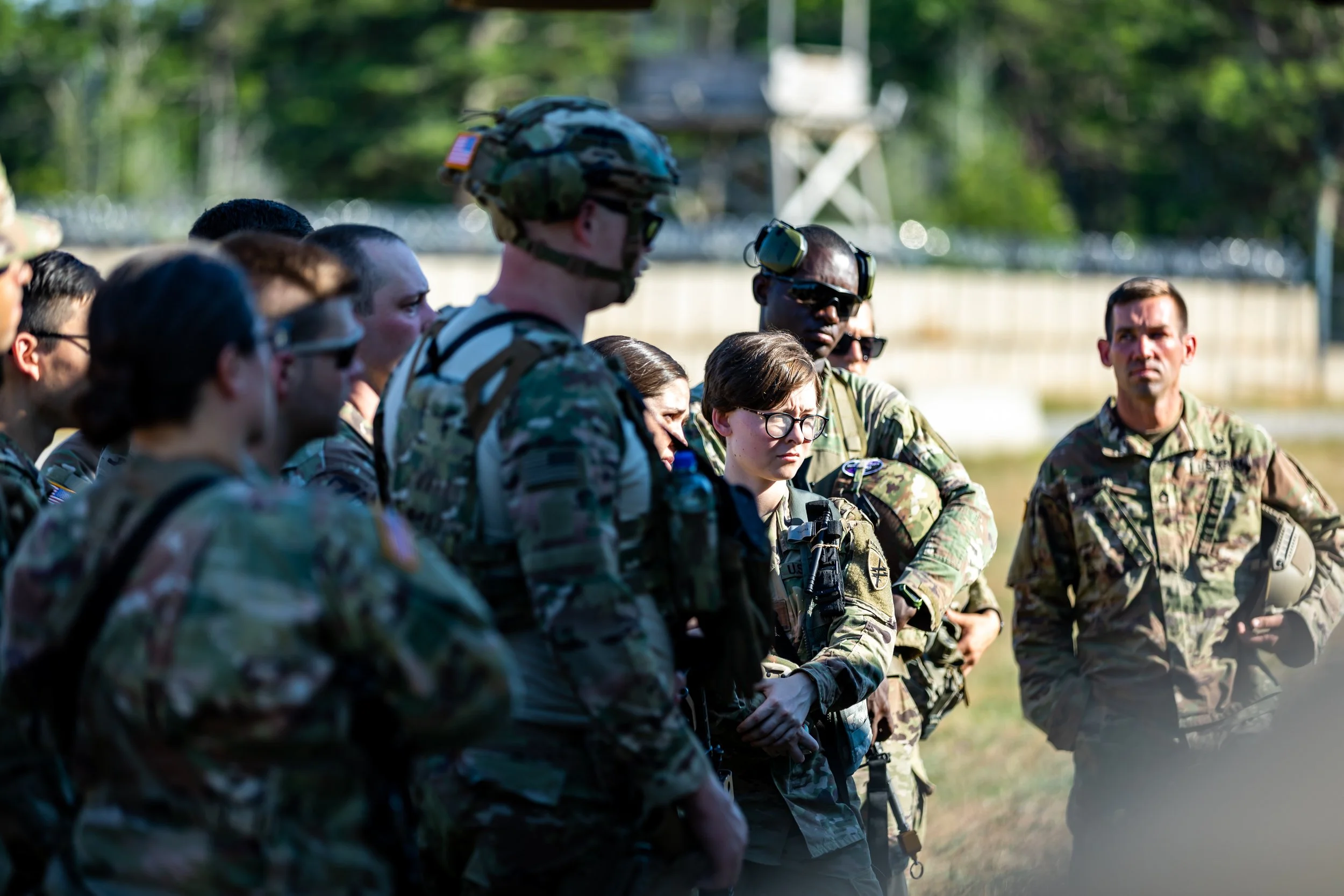 Group of military personnel in camouflage uniforms standing outdoors in a briefing or discussion.