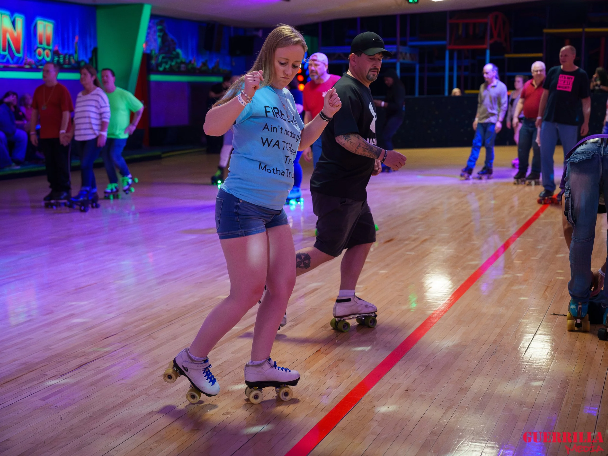 People roller skating in an indoor rink, with neon lights and colorful walls.