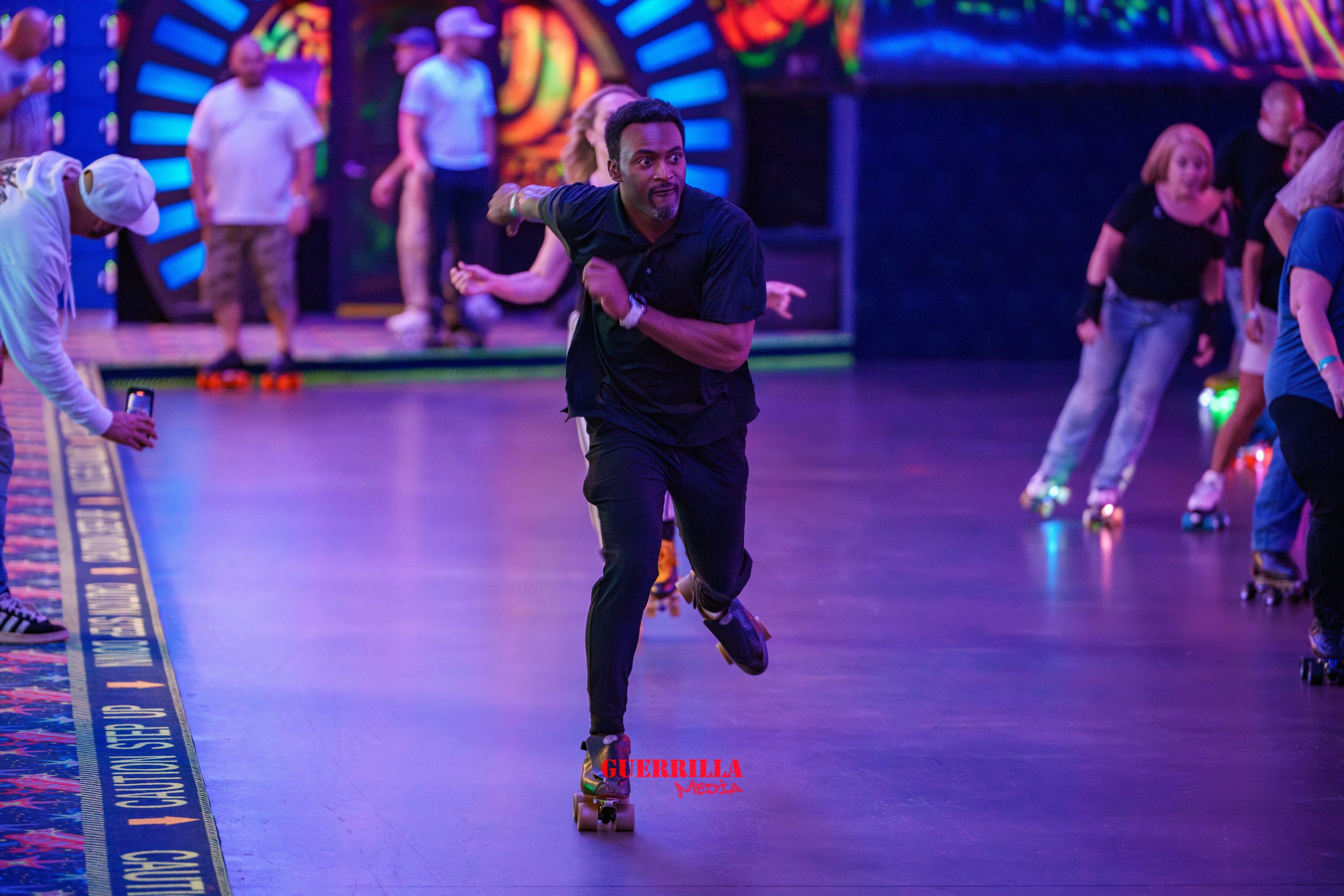 A man roller skating indoors at an entertainment venue with neon lights, surrounded by other skaters and spectators.