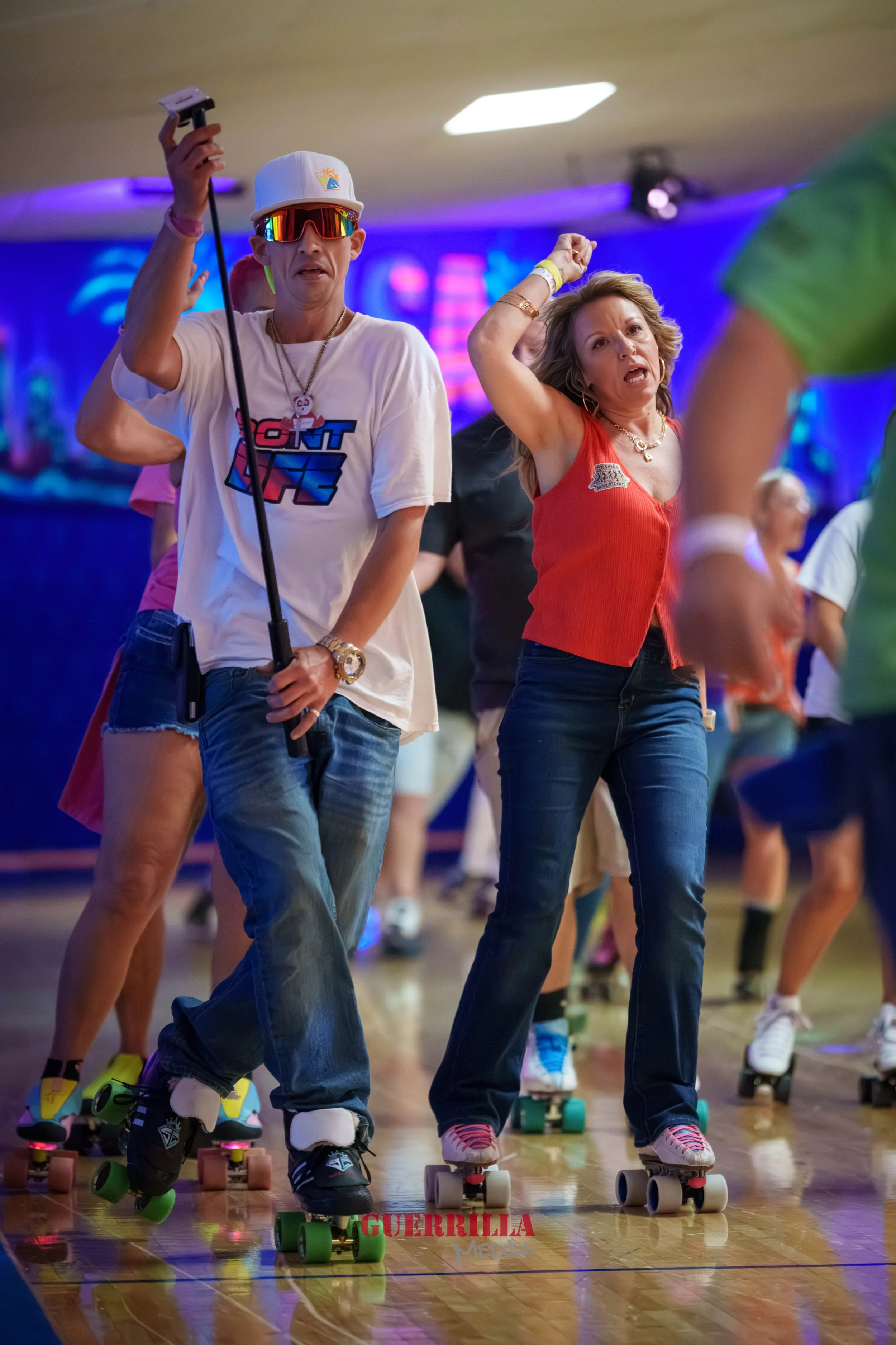 People roller skating indoors, two women dancing energetically, surrounded by others on skates, colorful lighting, lively atmosphere.