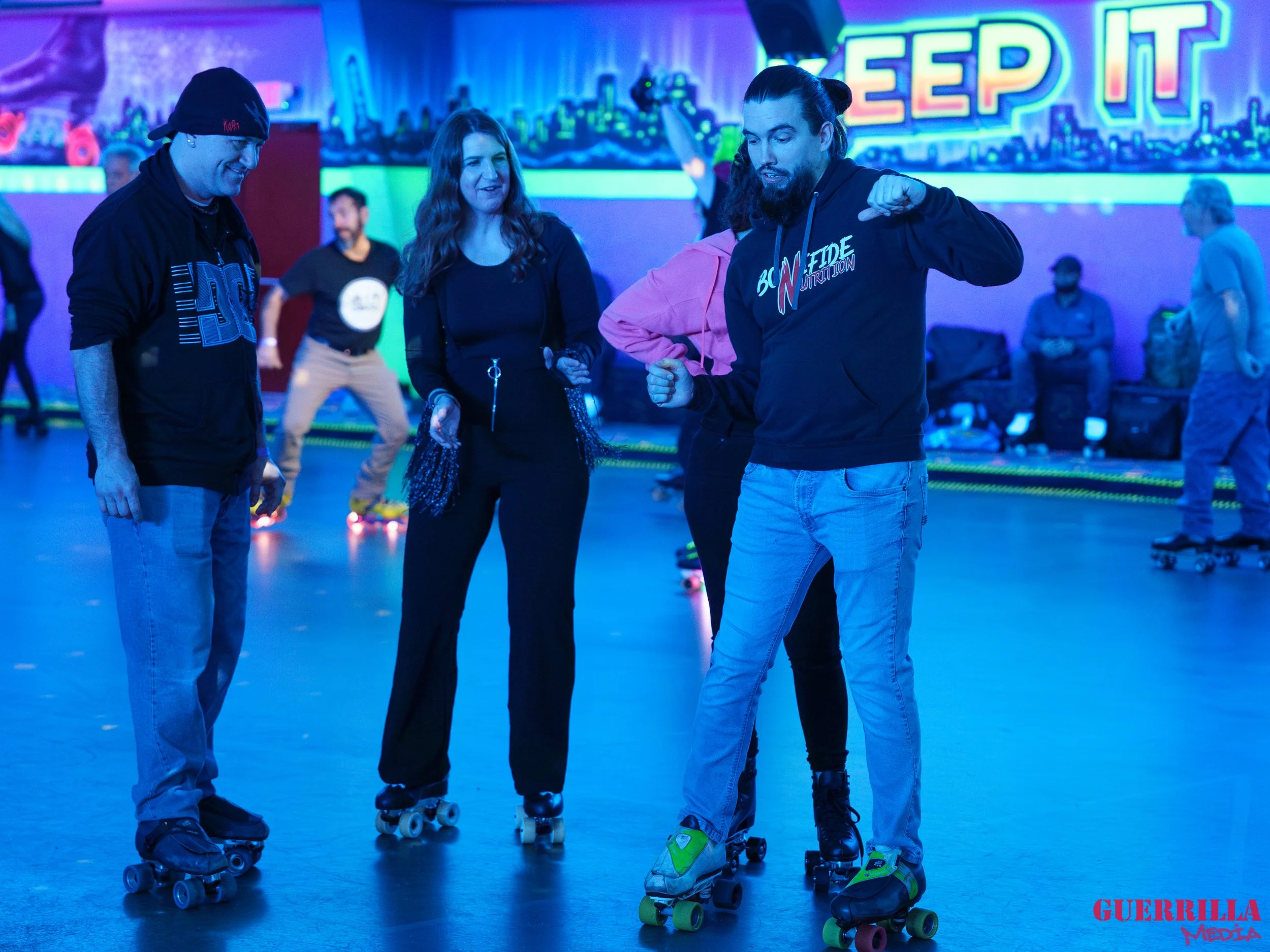 Group of people roller skating in an indoor rink with neon lights and a 'Sleep It' sign on the wall.