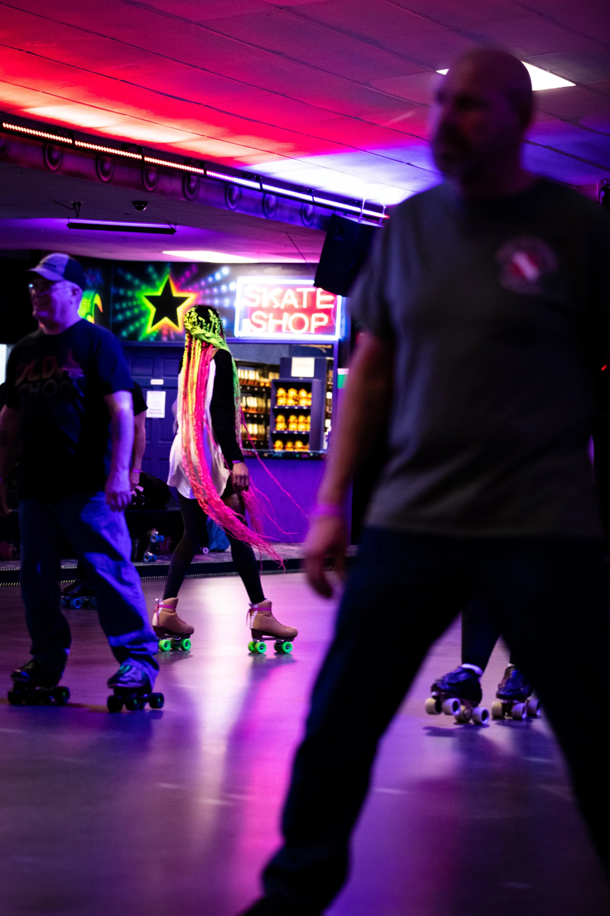 People roller skating in a neon-lit rink with a colorful sign in the background.