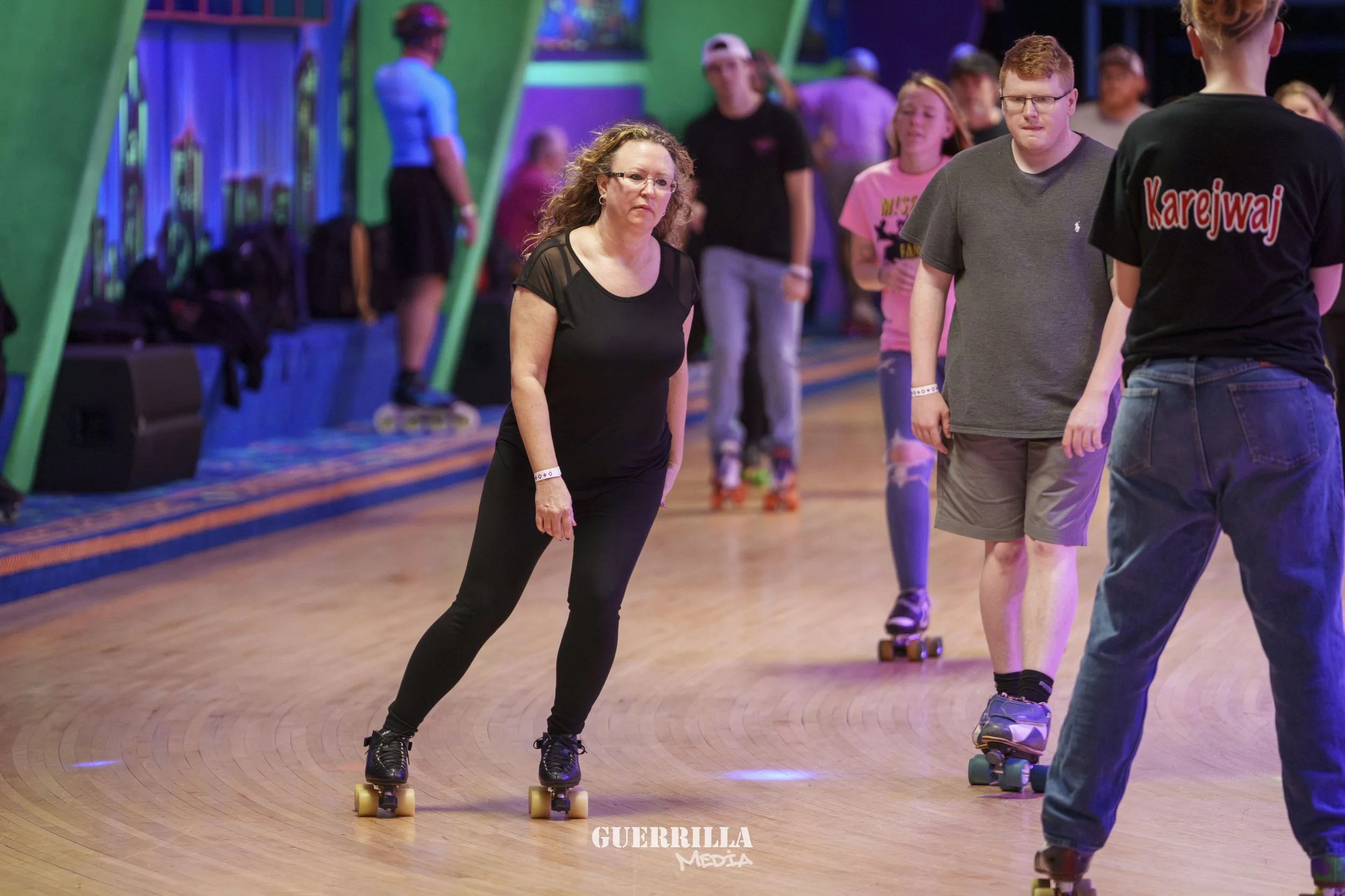 People roller skating indoors at an amusement or skating rink with colorful lighting and.