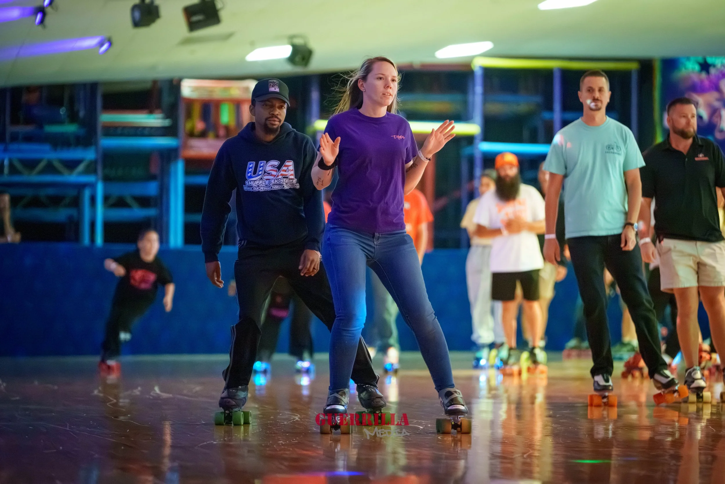 People roller skating at an indoor rink with colorful neon lighting and a climbing structure in the background.