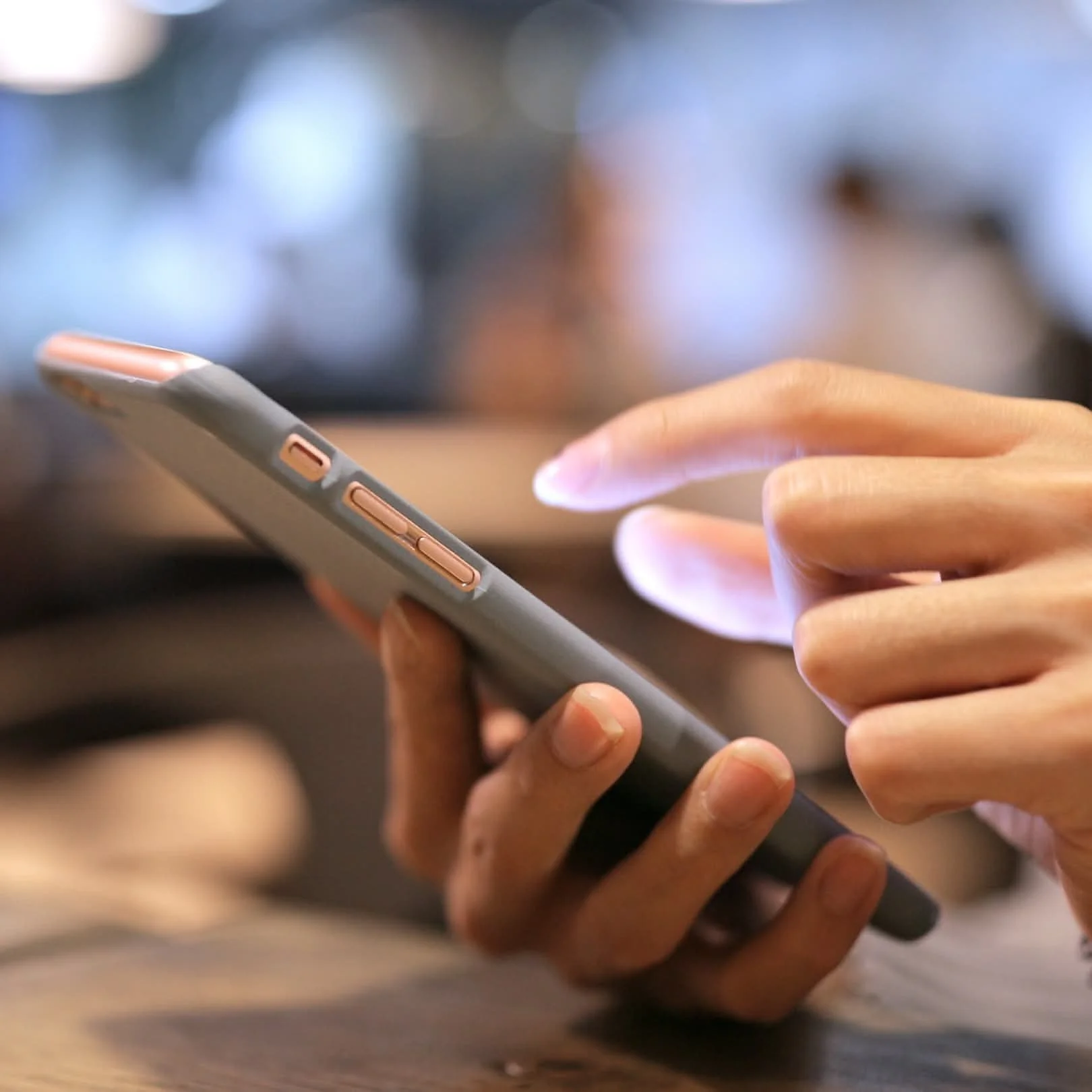 Close-up of a person using a smartphone with a gray and pink case, with one finger touching the screen.