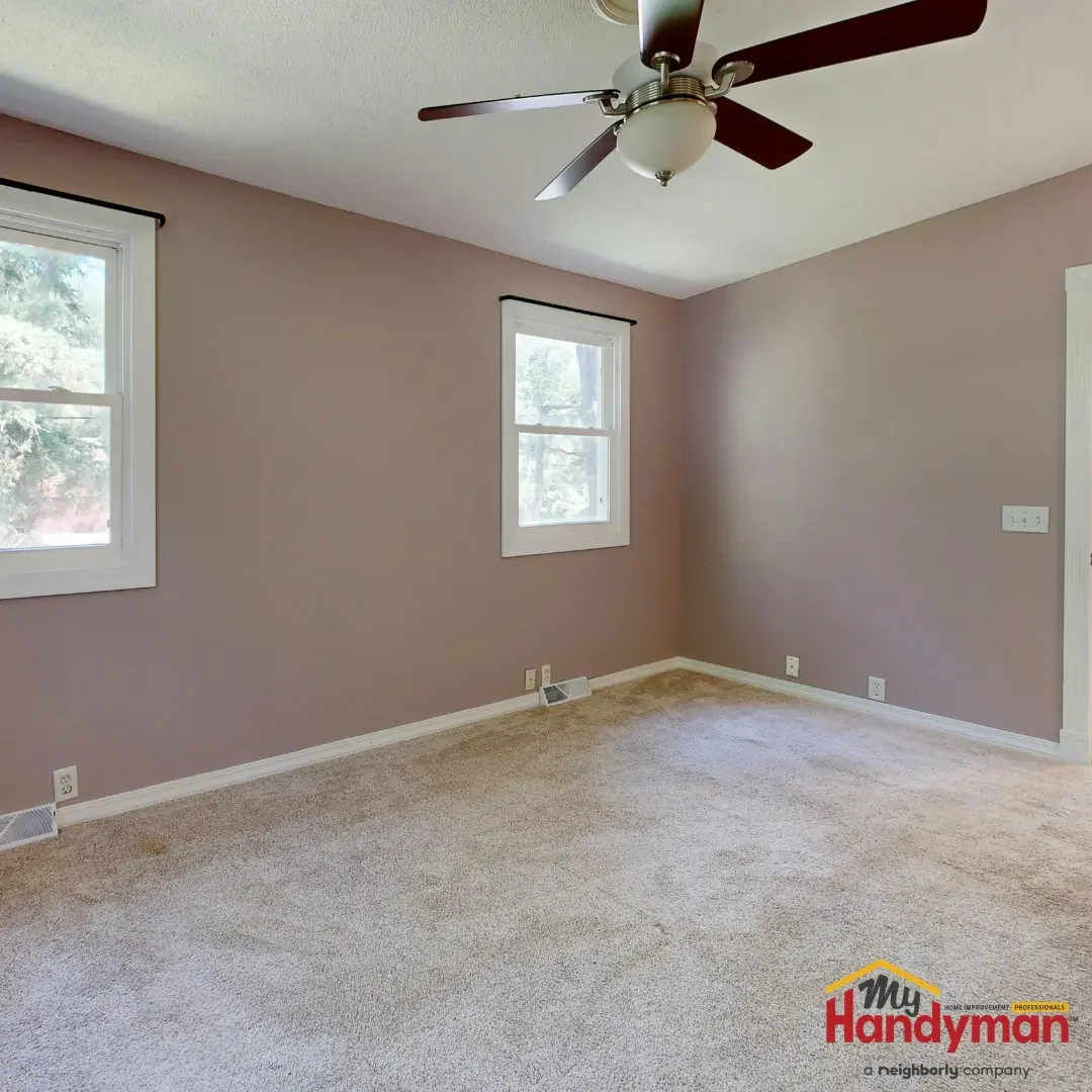 An empty room with freshly painted mauve walls, white baseboards and window trim, a ceiling fan, and carpet in a Chelsea, Michigan home.