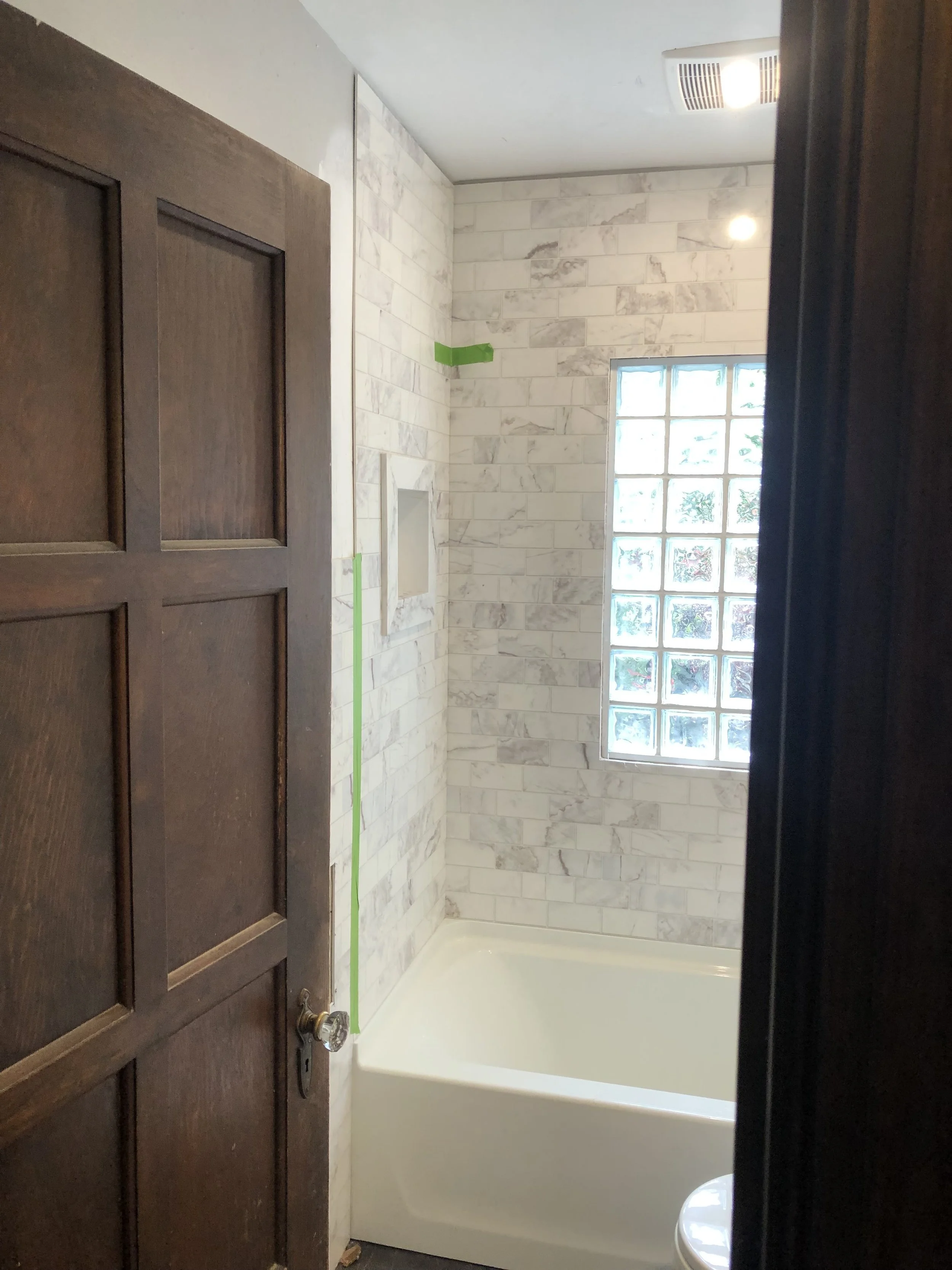 Bathroom tile installation with built-in shower niche, glass block window, and modern wall tile.