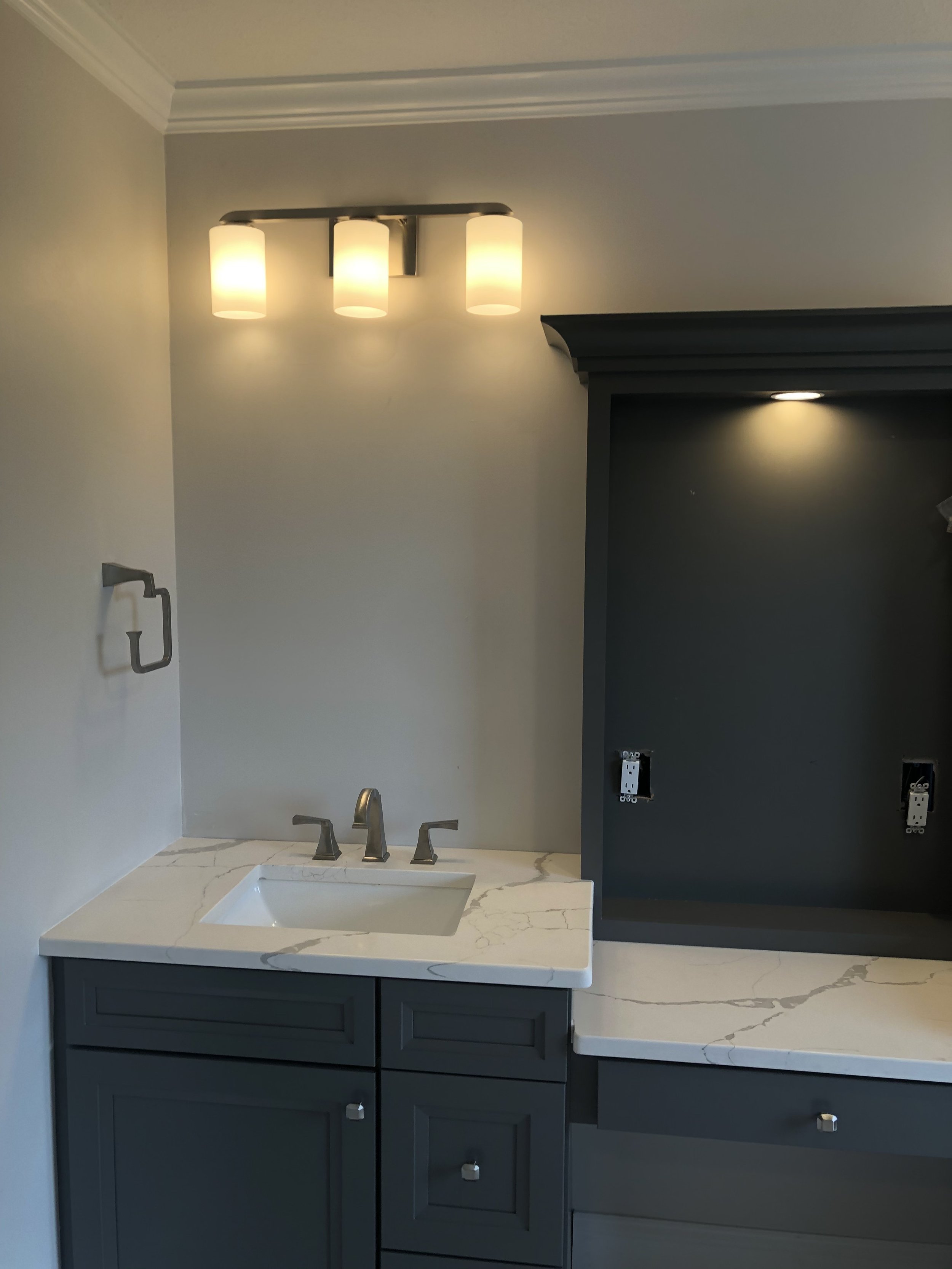 Modern bathroom vanity installation featuring quartz countertops, sleek dark cabinetry, and updated lighting fixture.