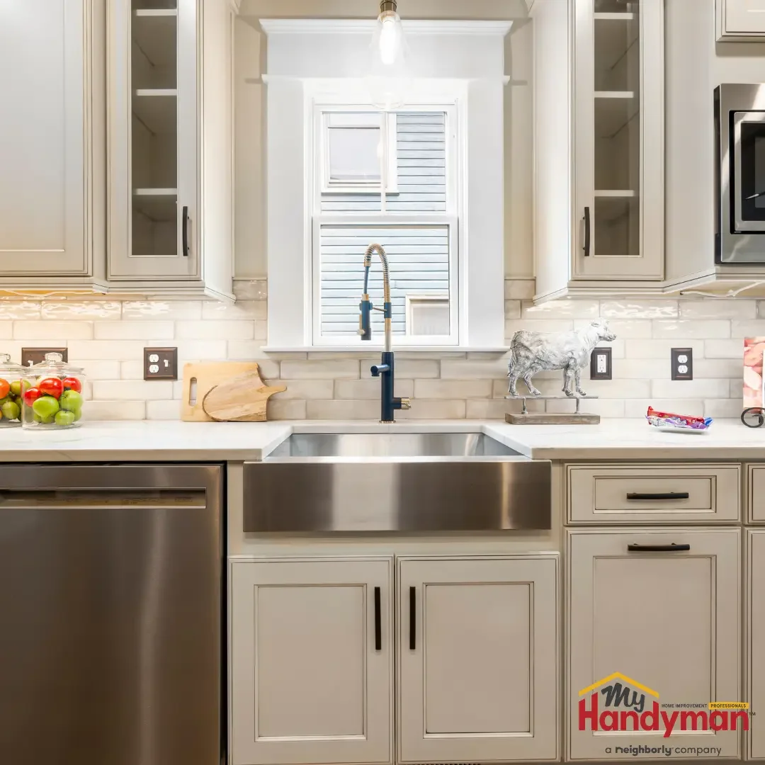 A stainless farmhouse kitchen sink with a pull-down faucet, a built-in dishwasher to the left, and a tiled backsplash in an Ann Arbor, Michigan kitchen.