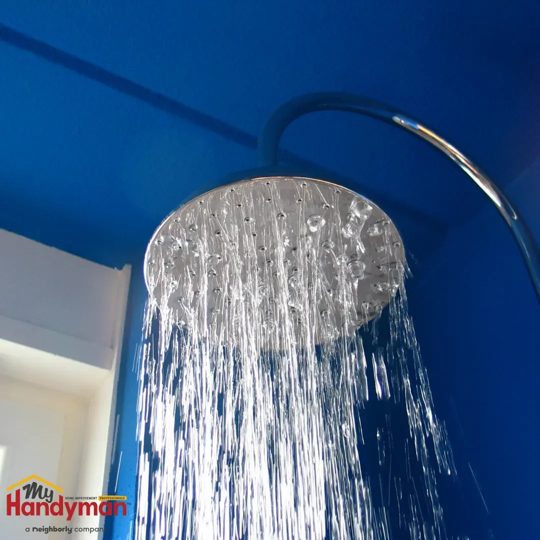 A round chrome rain showerhead on a curved arm delivering a full, even spray against a deep blue bathroom wall in an Ann Arbor, Michigan home.