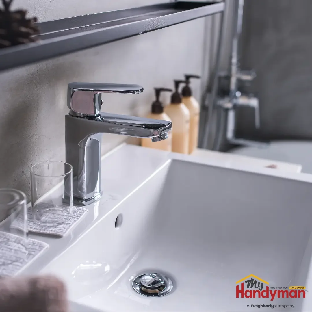 A modern single-handle chrome bathroom faucet on a white rectangular sink, with soap dispensers and a glass nearby, in an Ann Arbor, Michigan bathroom.