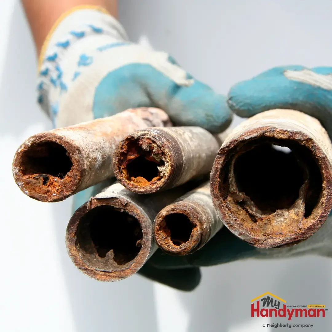 A gloved hand holding several cut sections of old galvanized steel pipe with heavy rust and mineral buildup narrowing the interior, from an older Ann Arbor, Michigan home.