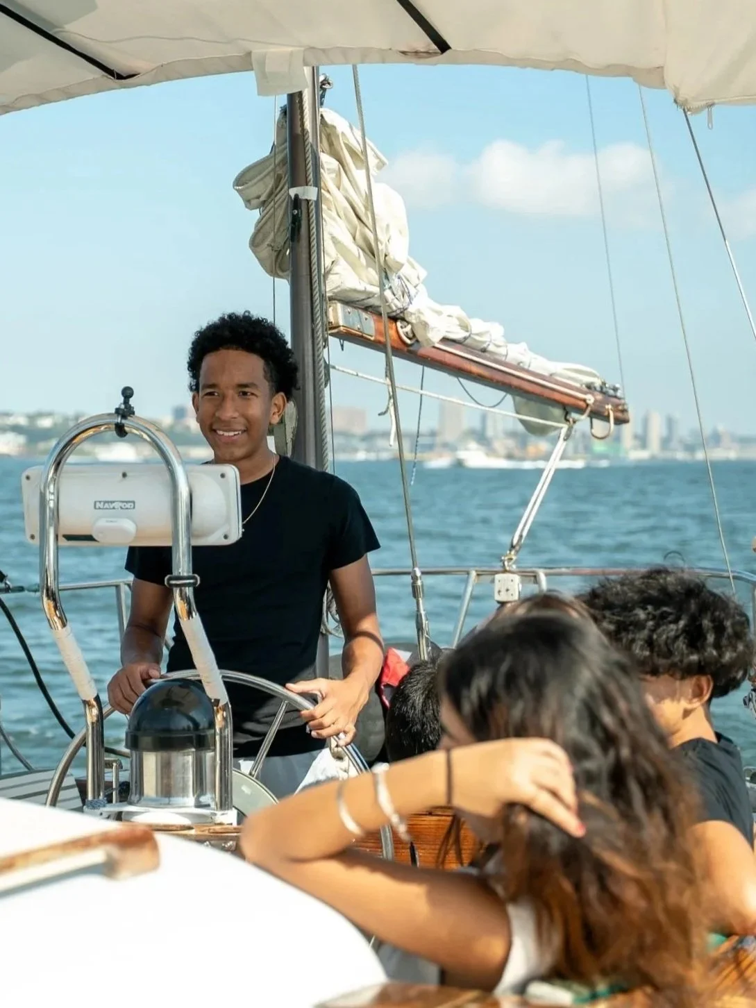 A group of people on a boat enjoying a day on the water, with one person steering and others relaxing.