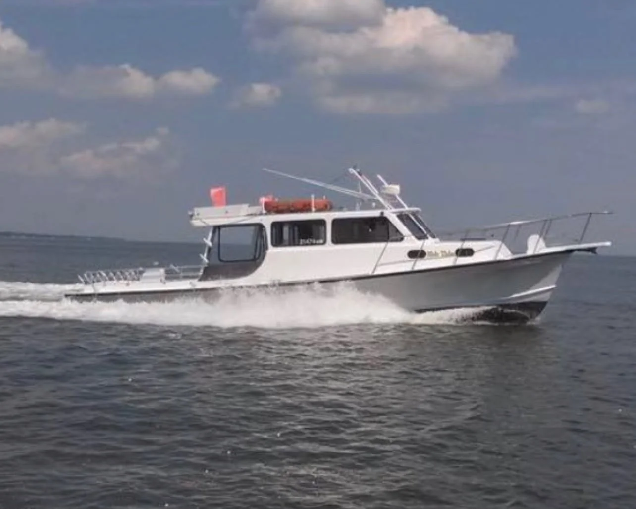 A white motorboat speeding through the water on a clear day with scattered clouds in the sky.