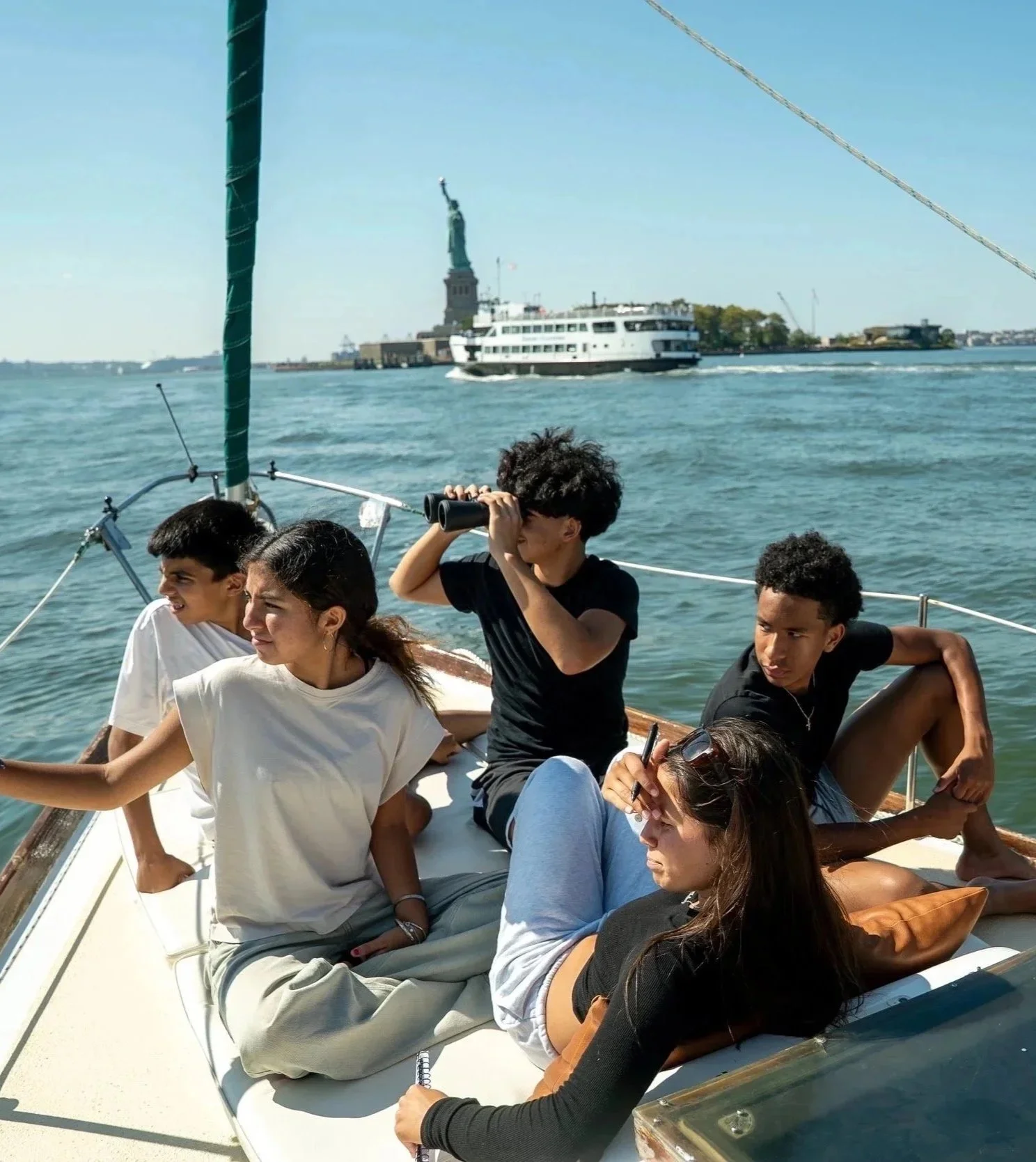 Group of young people relaxing on a boat with the Statue of Liberty in the background.