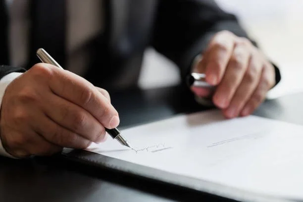 Person in a suit signing a document with a pen