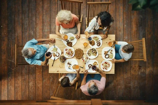 Top view of six people gathered around a wooden dining table enjoying a meal together.