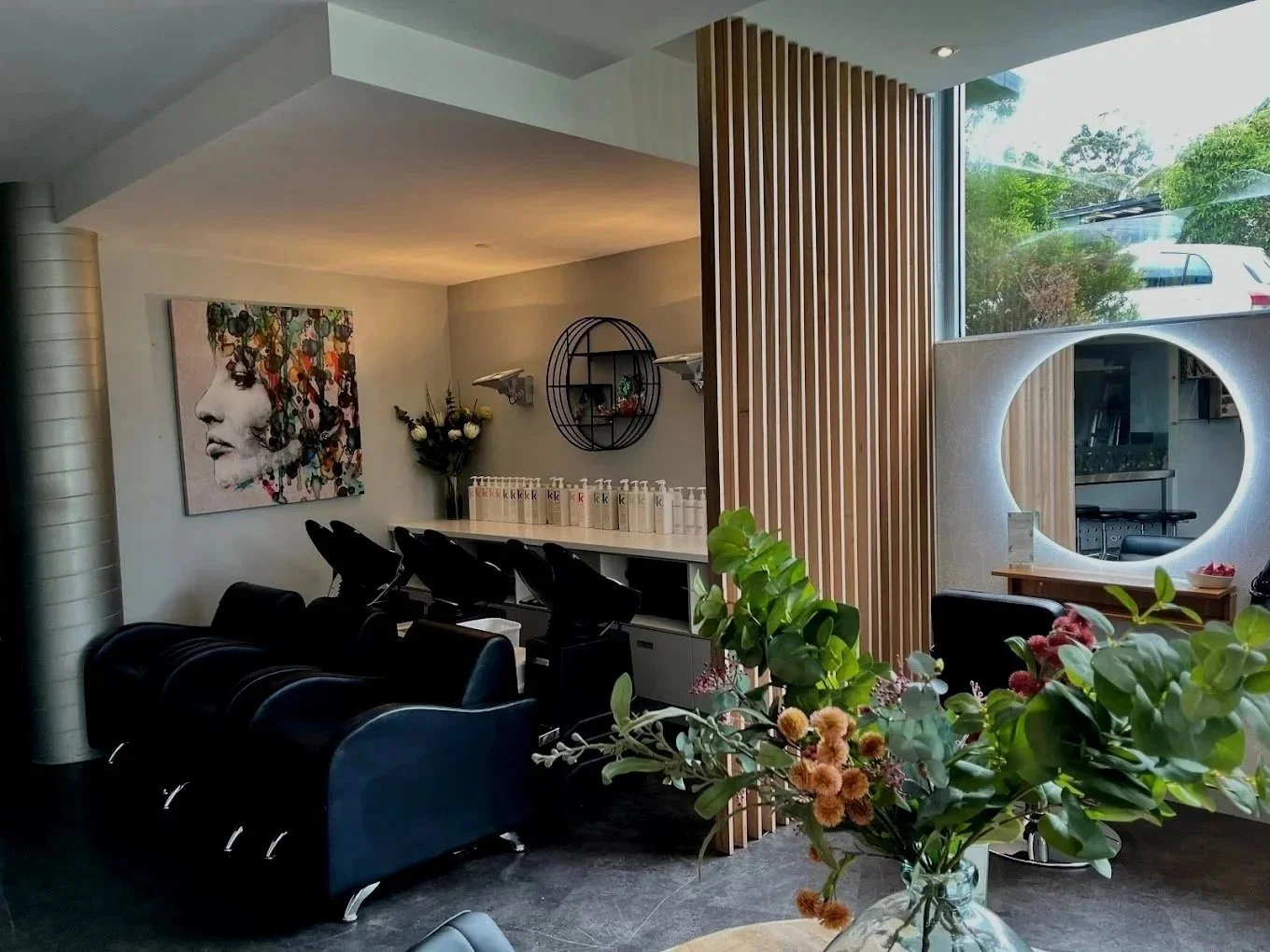 Interior of a hair salon with black salon chairs, a large eye-shaped mirror, and abstract artwork on the wall.