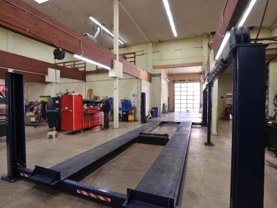 An automotive lift in a spacious garage or workshop, with tools and equipment on the sides and a large garage door at the back.