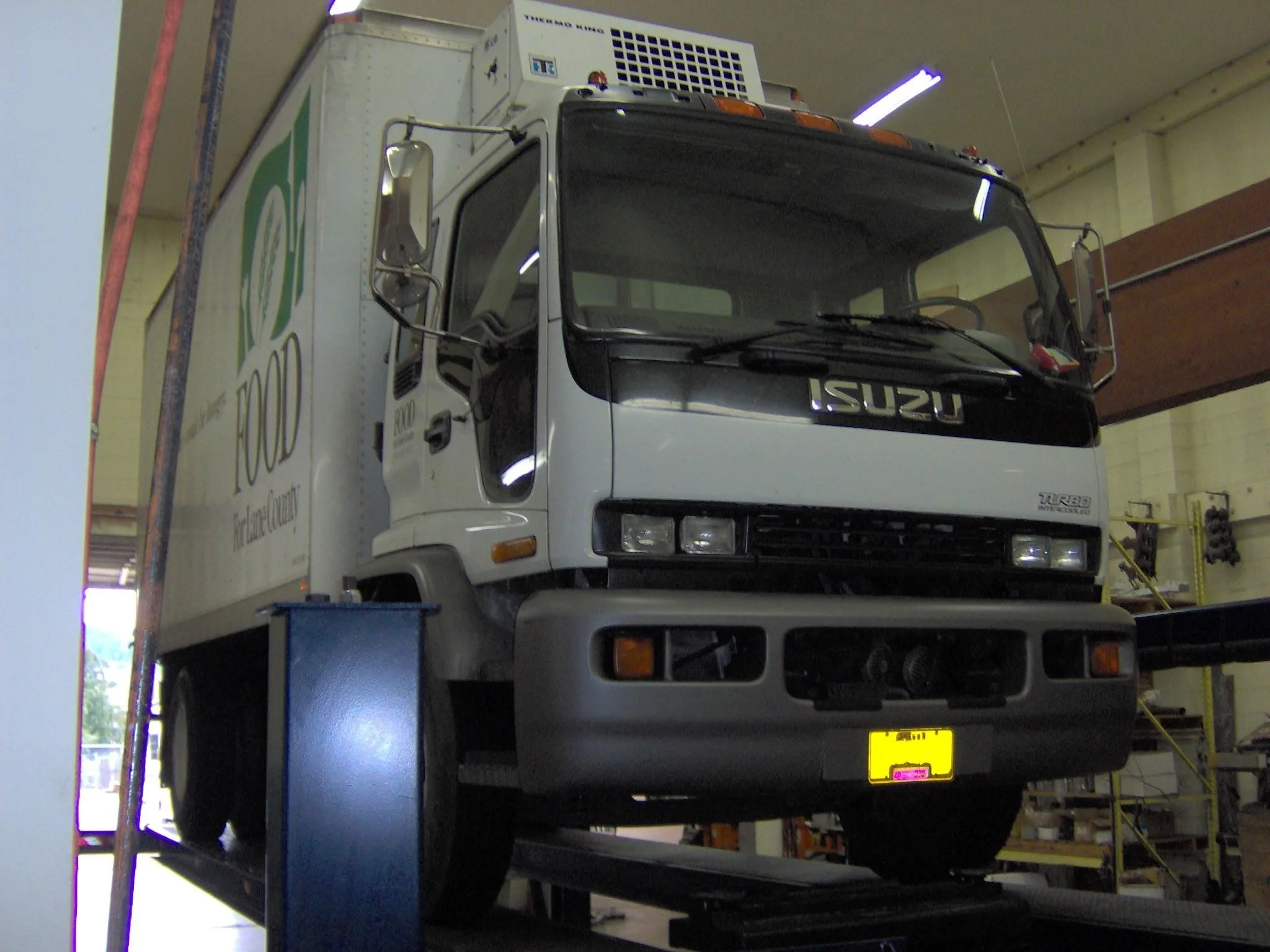 Front view of an Isuzu delivery truck inside a warehouse or garage, elevated on a lift.