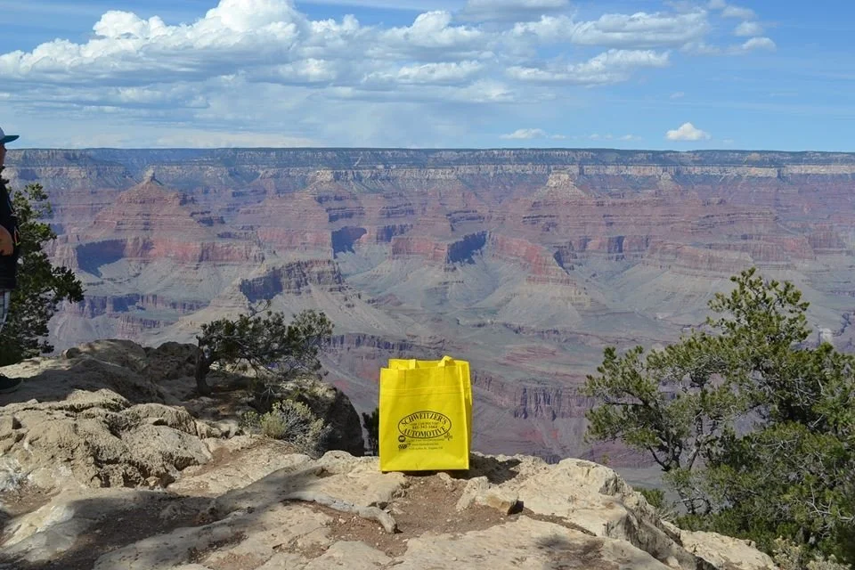 View of the Grand Canyon with a yellow tote bag on the rocky ledge in the foreground, cloudy sky overhead.