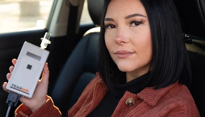 Woman sitting in car holding a breathalyzer device.