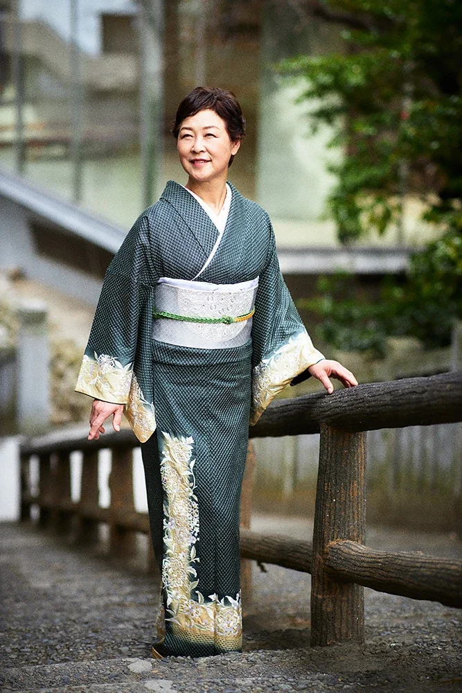 着物を着た女性が木の柵にもたれて立っている写真