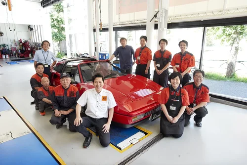 赤いフェラーリ車とスタッフのグループ写真