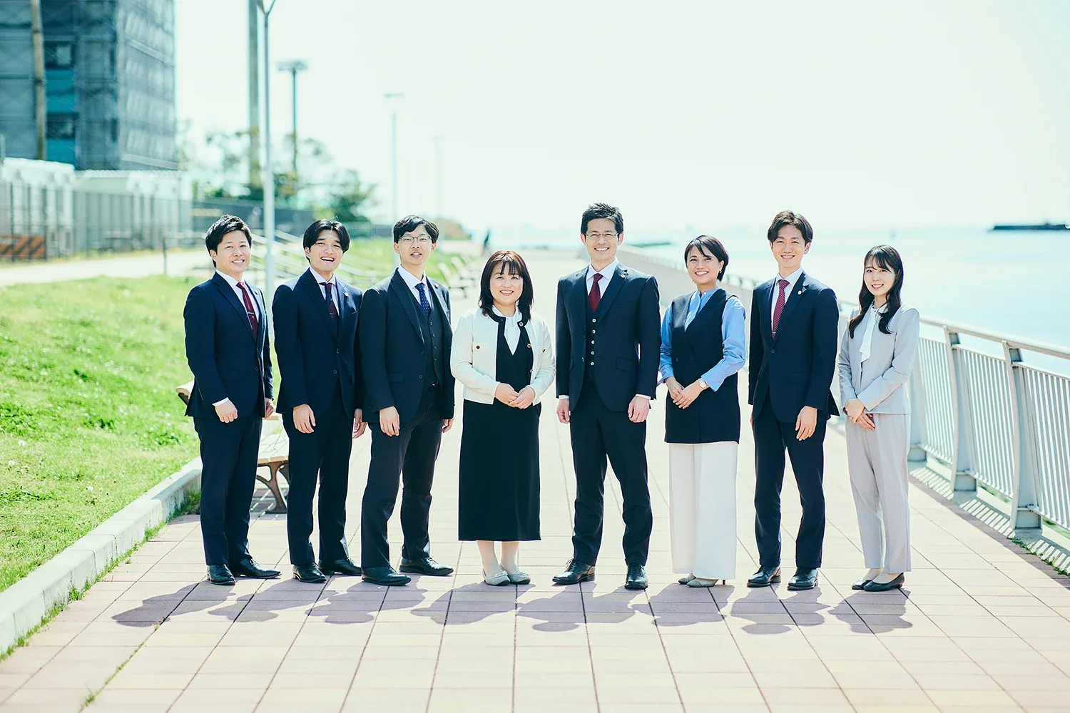 ビジネスマンとビジネスウーマンが海辺の散歩道で並んで笑顔で立つグループ写真