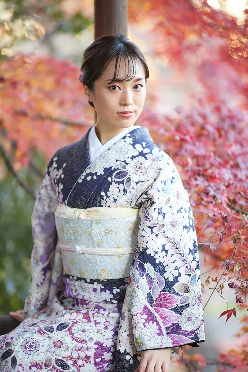 着物を着た若い女性が秋の紅葉の背景の中で座っている写真